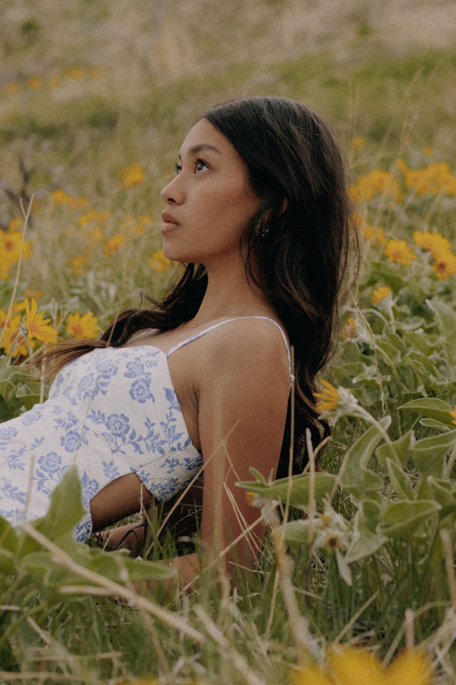 Woman in floral dress poses among yellow wildflowers in natural outdoor setting.