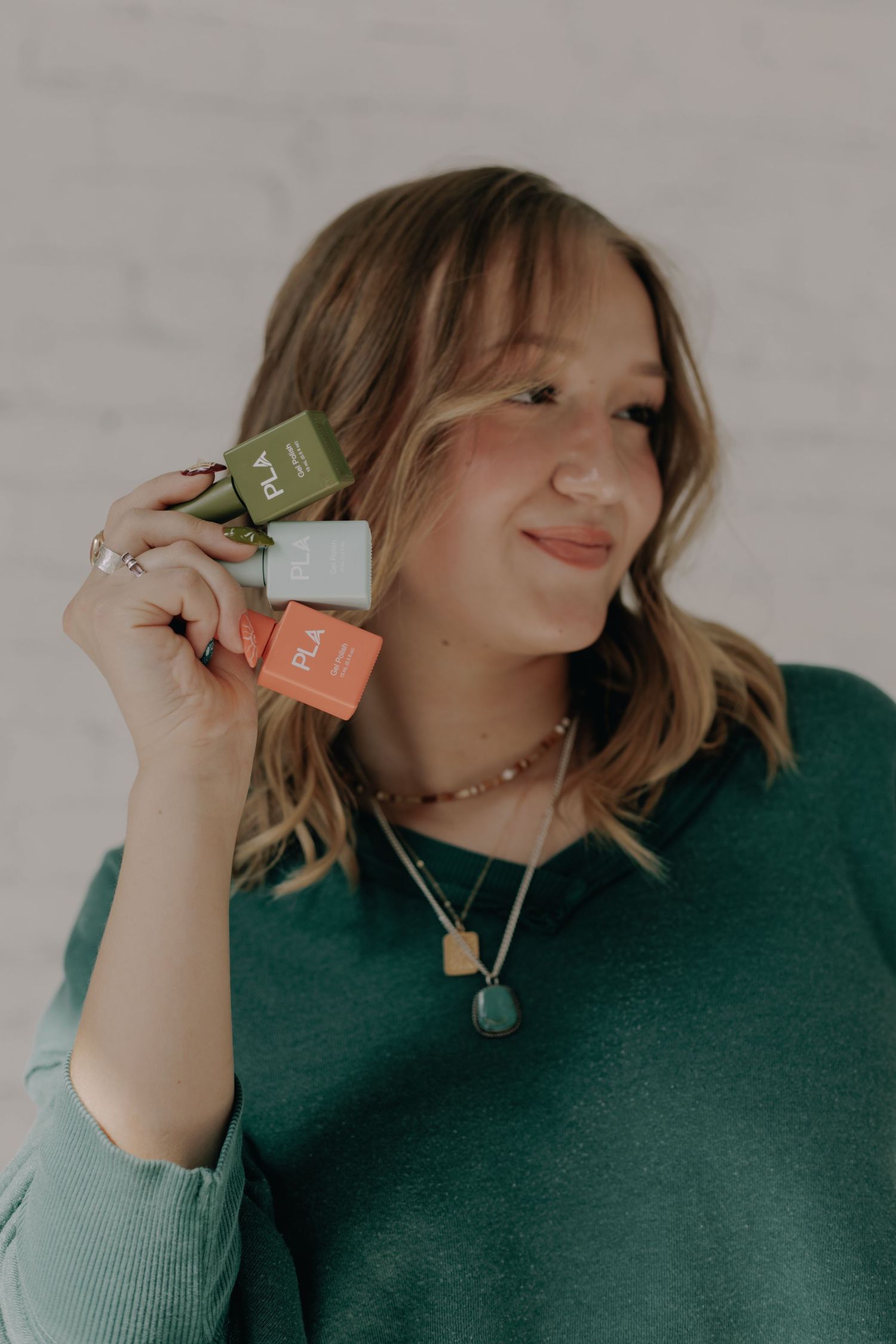 Person wearing emerald sweater displays small product bottles with a cheerful expression.