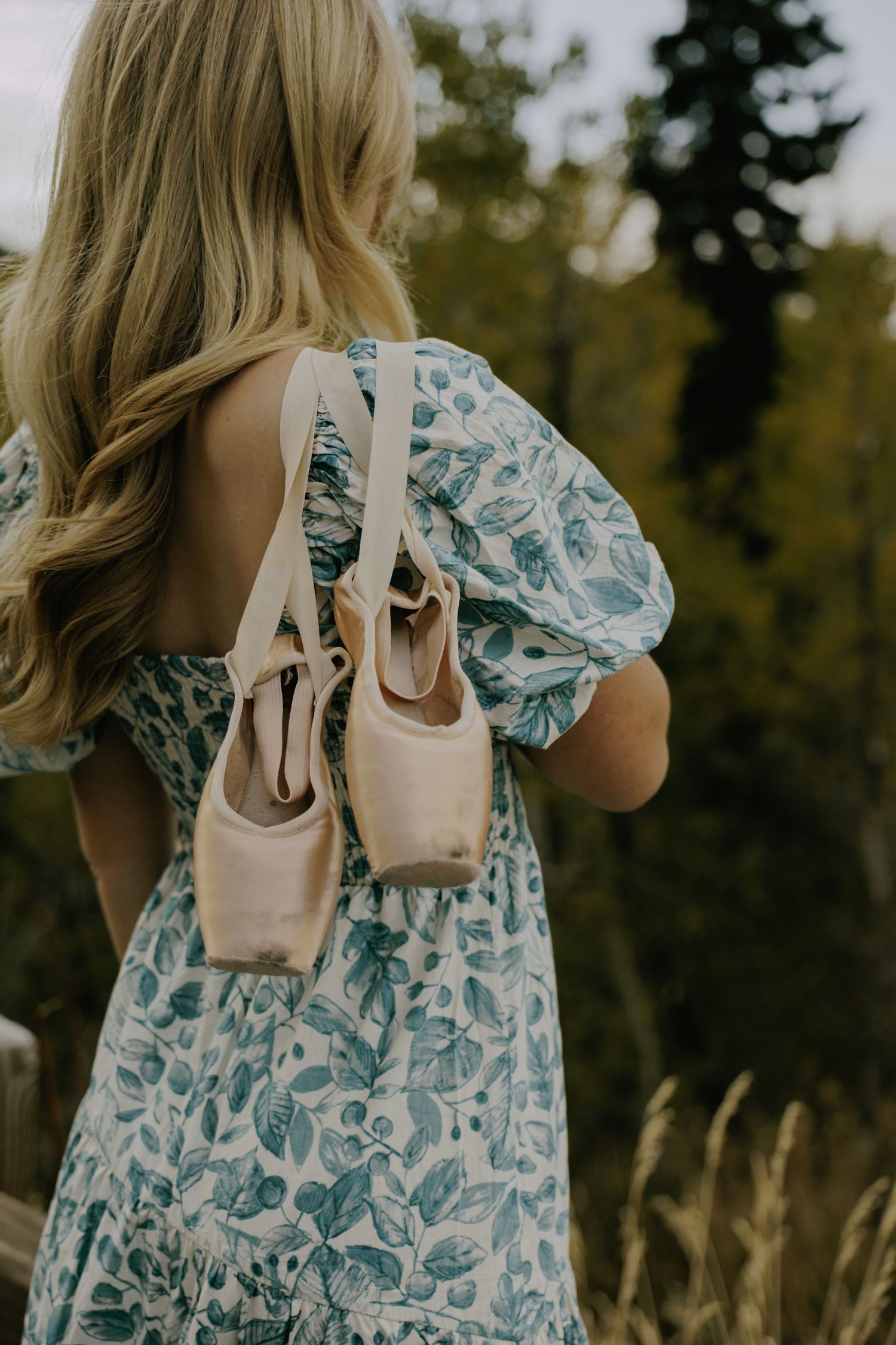 A light pink handbag complements a blue floral dress in an outdoor photoshoot.