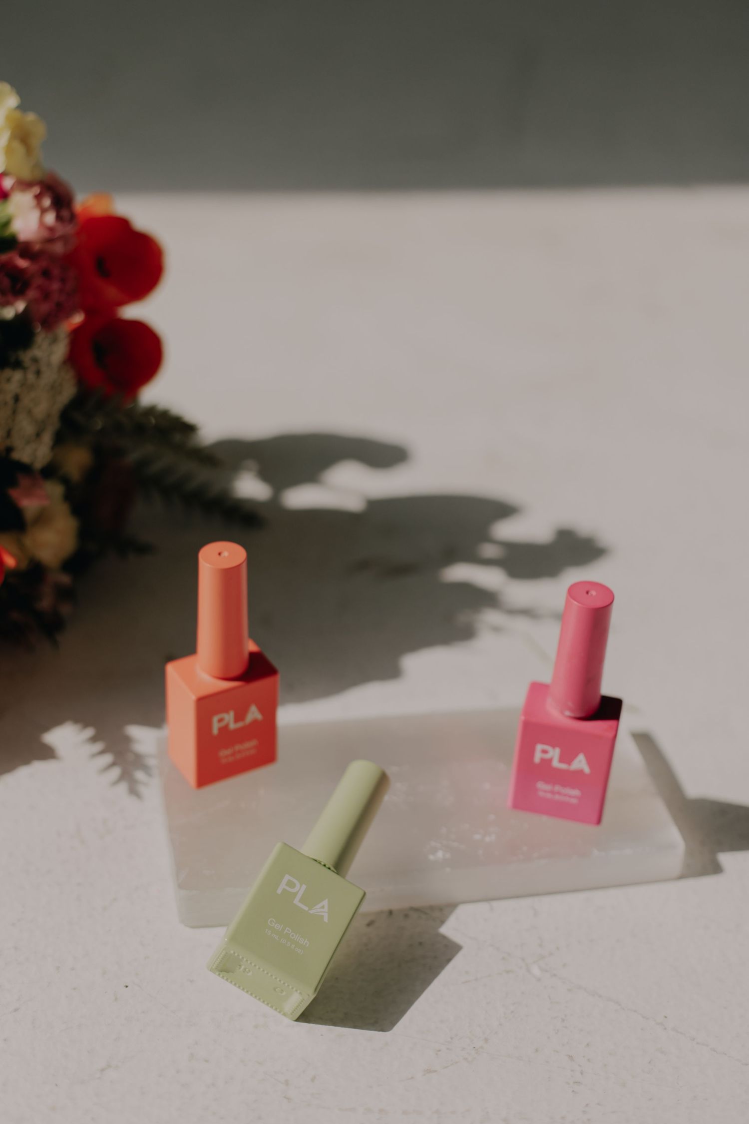 Colorful nail polish bottles arranged artistically with shadows and red flowers in background.