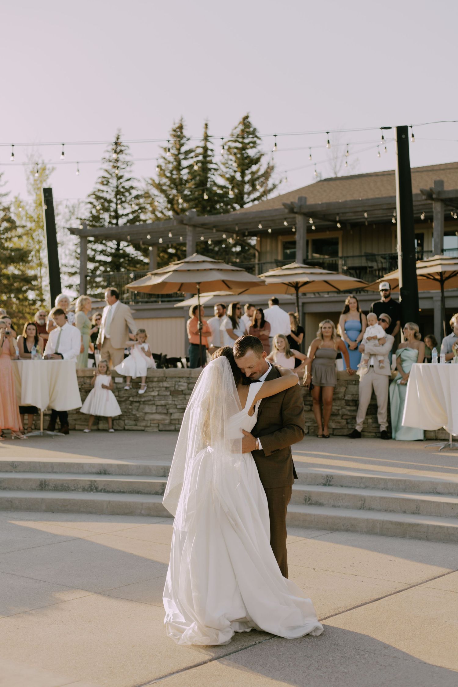Wedding couple dances surrounded by guests at outdoor reception venue.