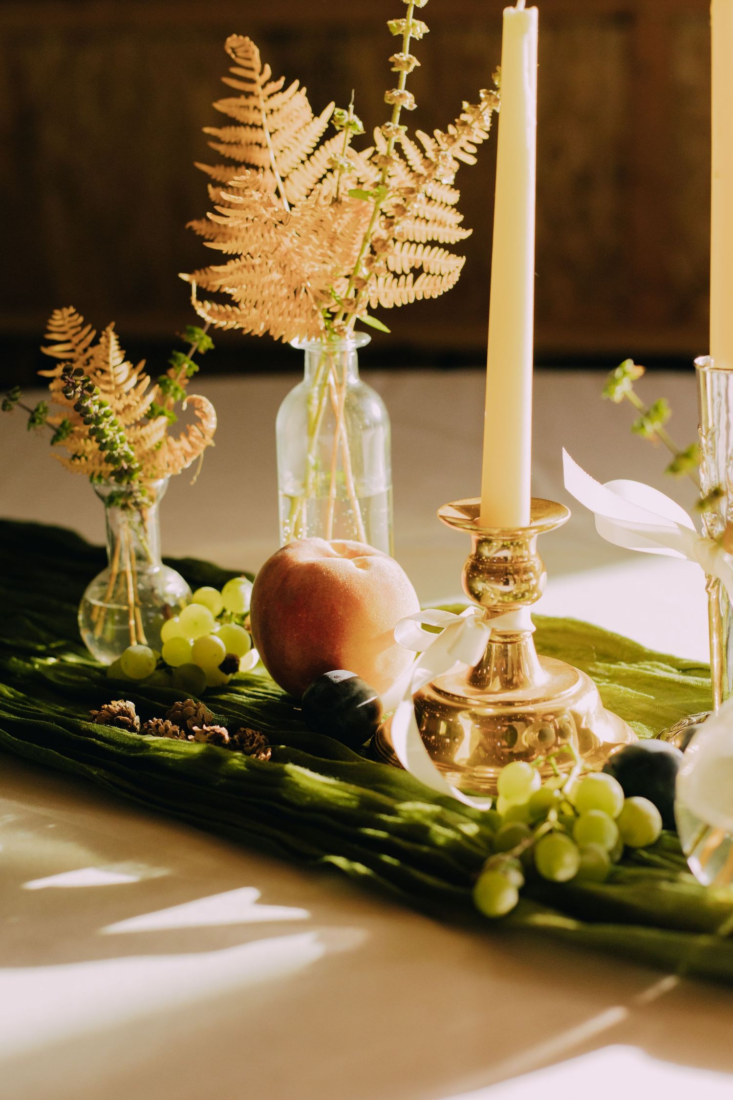 Elegant table setting with golden ferns, candles, and fresh grapes creating a romantic atmosphere.