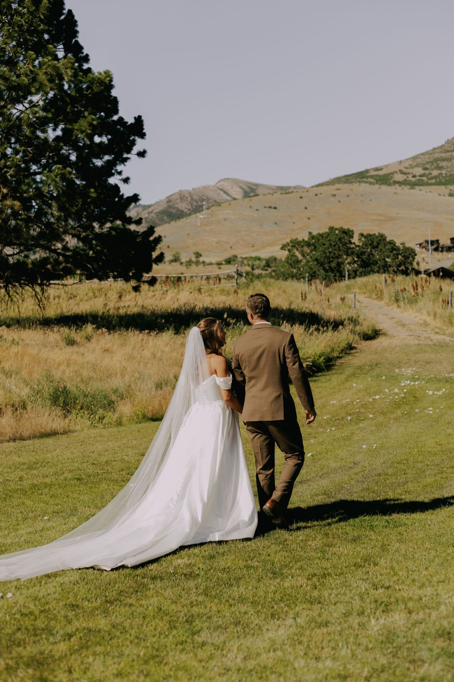 A couple walking on a grassy hill with a long flowing wedding dress train.
