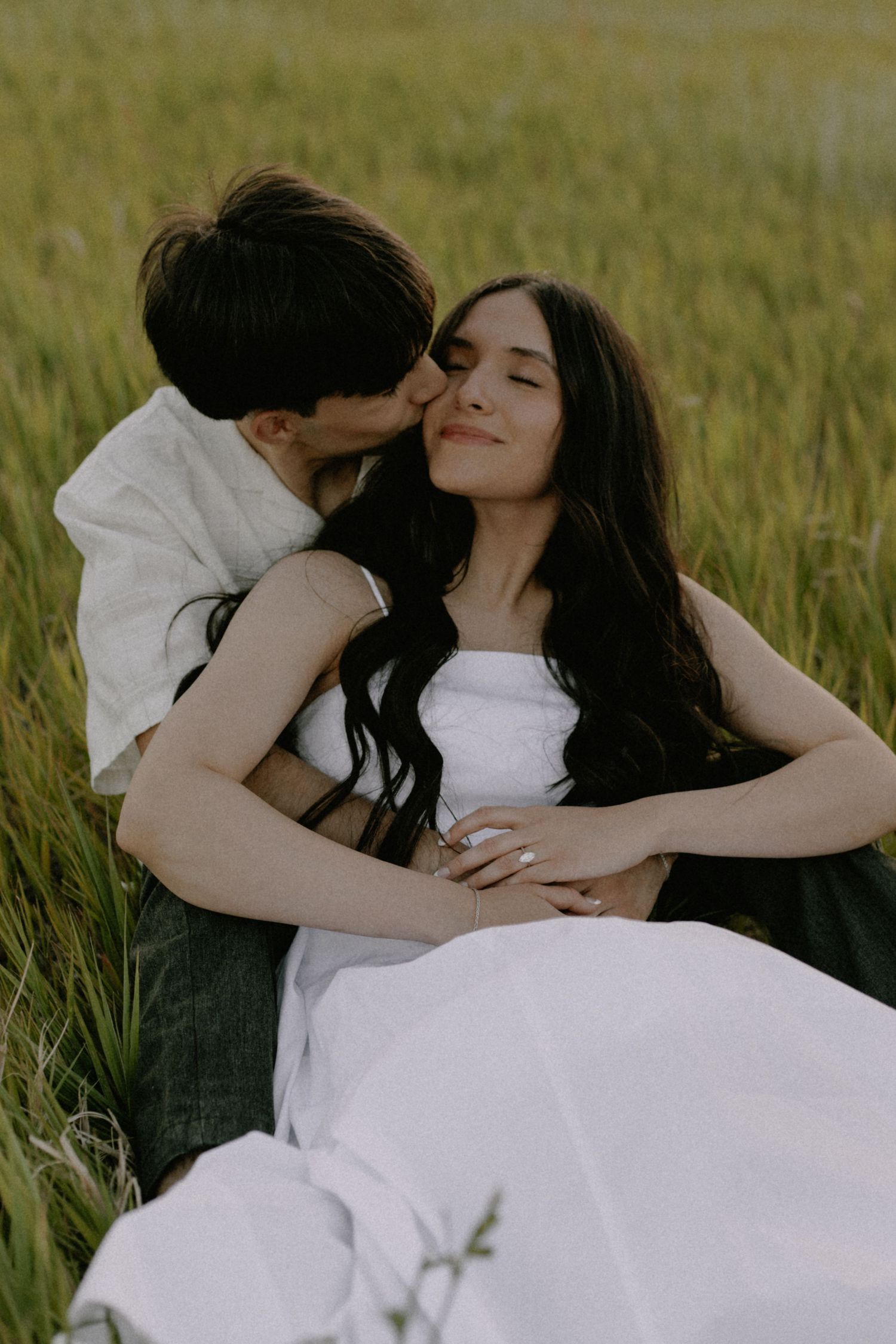 A romantic moment captured between two people lying in a sunlit meadow.