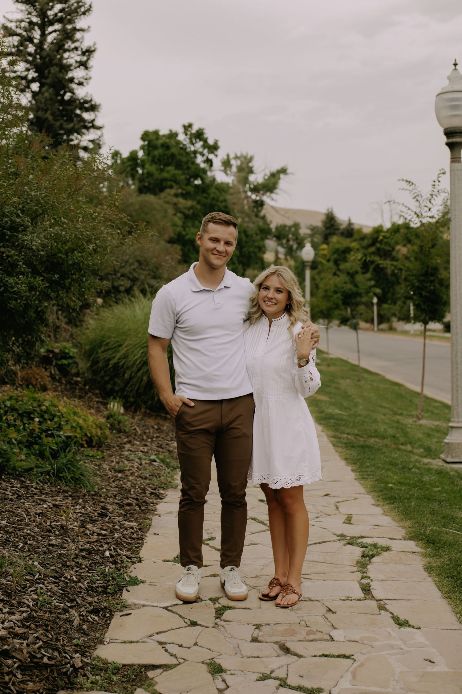 A couple walks together on a stone path surrounded by landscaped gardens.
