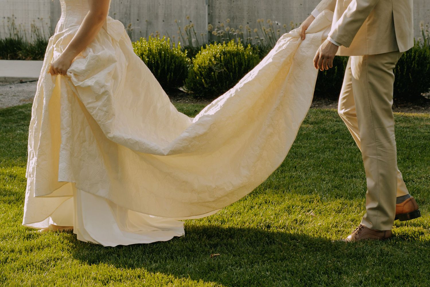 Wedding dress train flowing gracefully across green lawn.