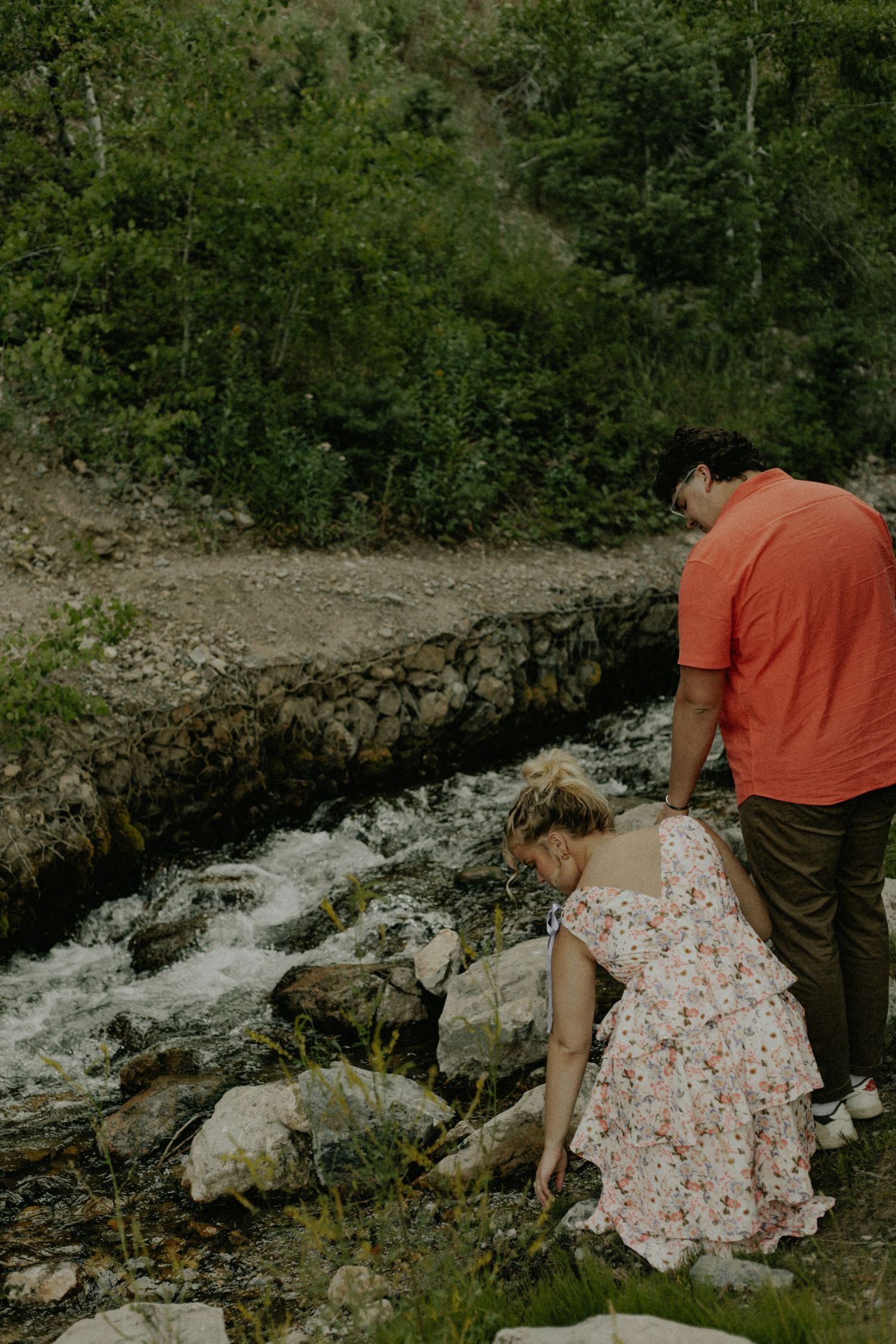 Two people exploring rocky terrain near a rushing waterfall.