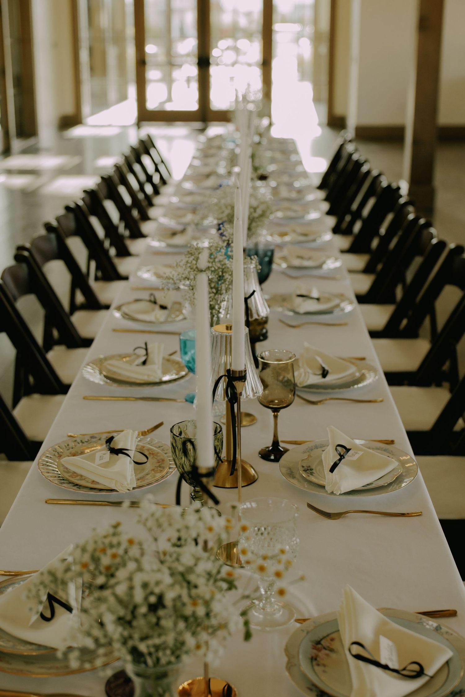 Elegant wedding reception table setting with white linens, black chairs and baby's breath centerpieces.