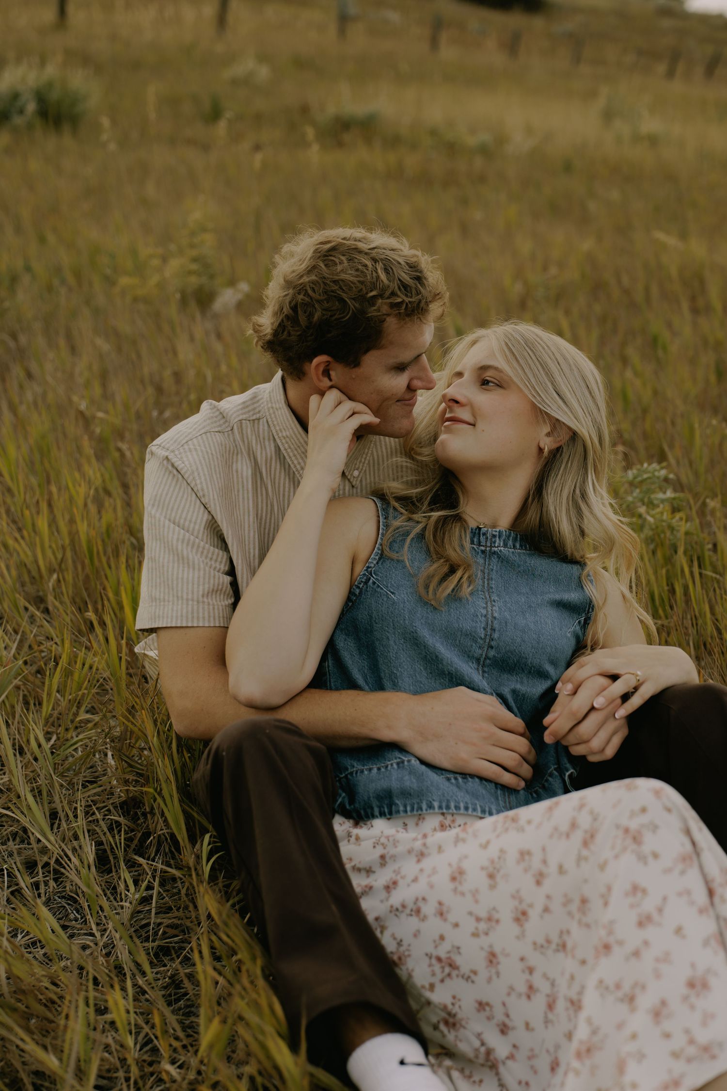 A couple shares tender moments while lying in tall grass at sunset.
