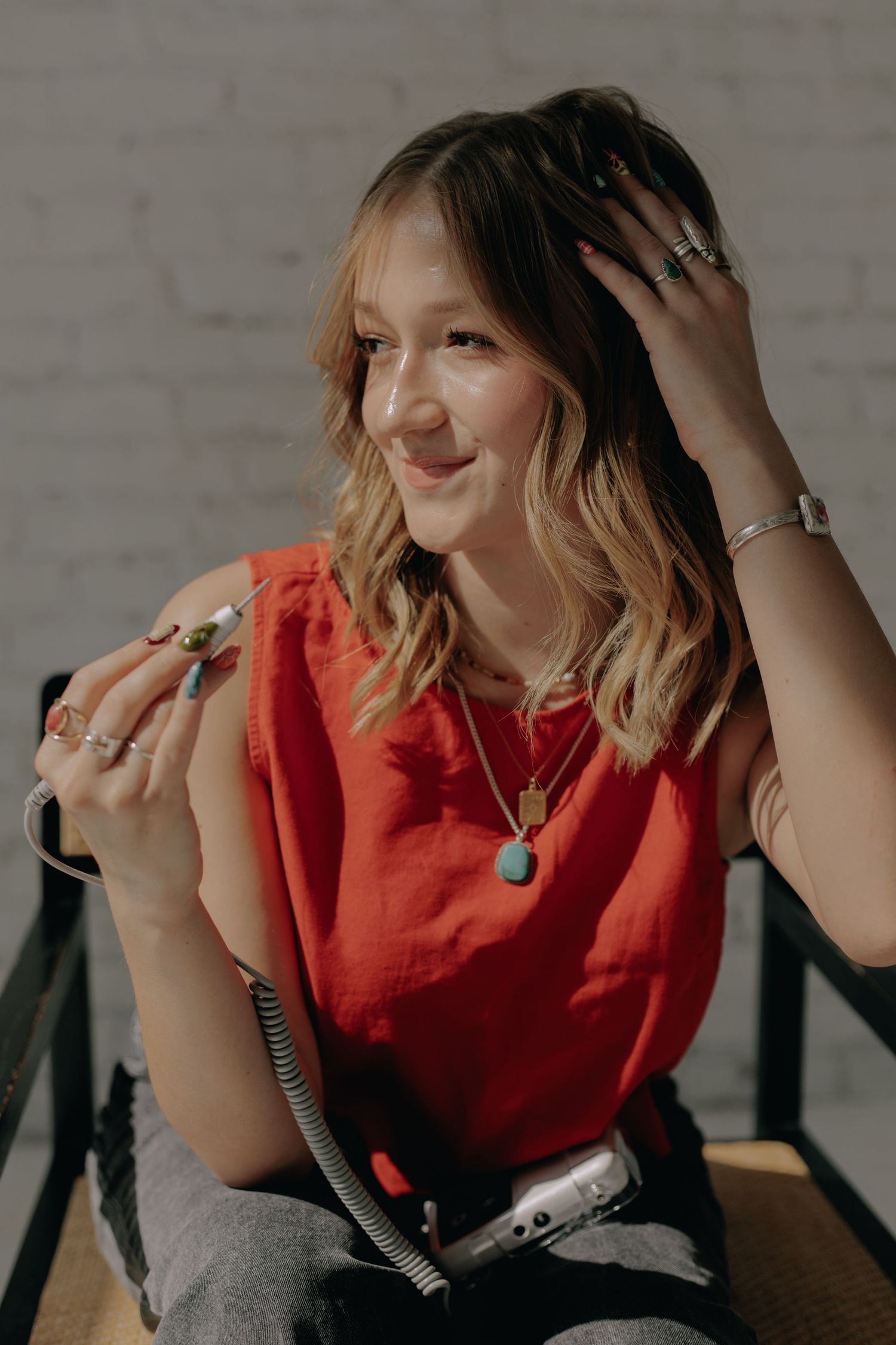 Fashion portrait showing someone in a vibrant red top with wavy blonde hair against a white brick wall background.