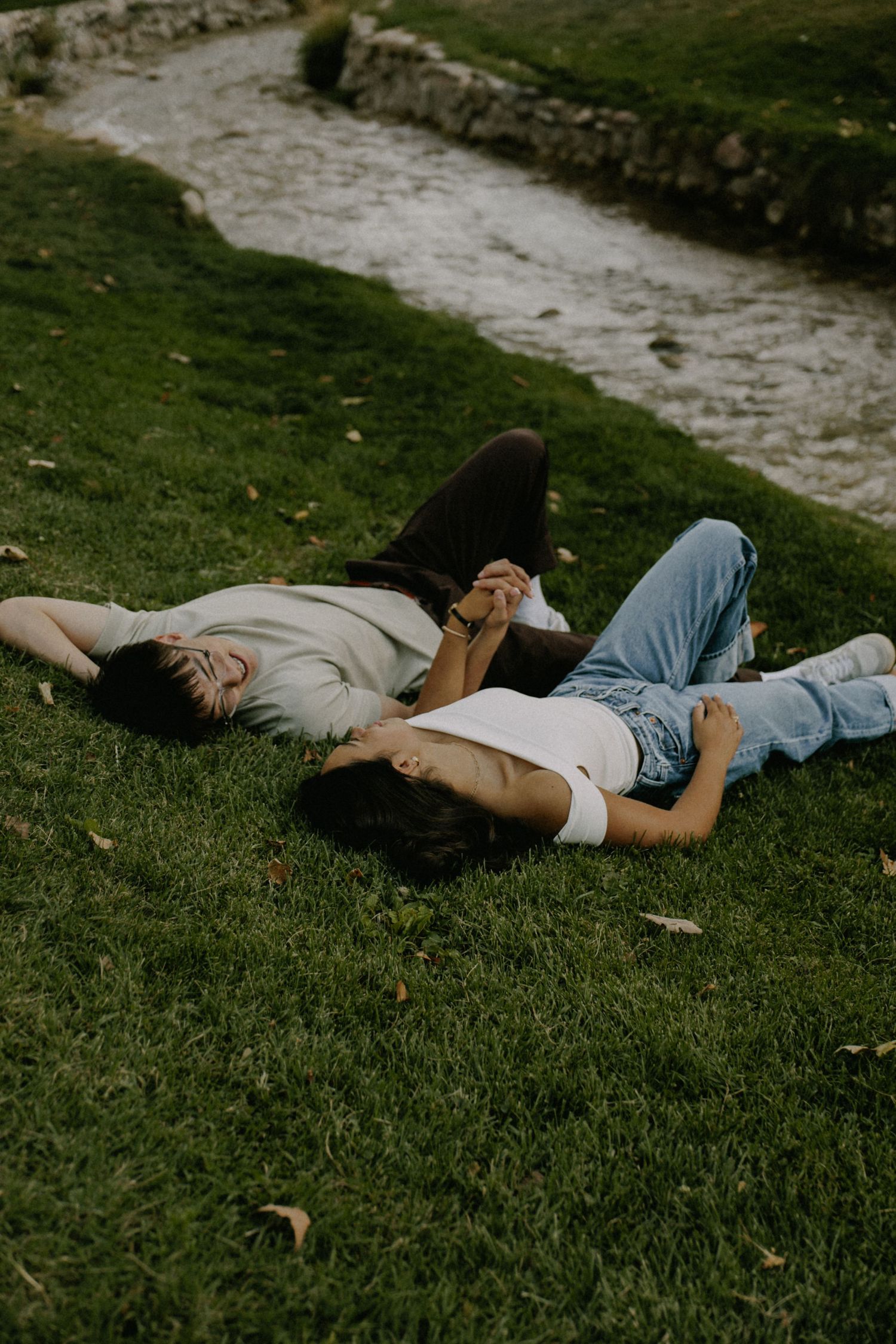 People lying down and relaxing on a lush green lawn next to a stone path.