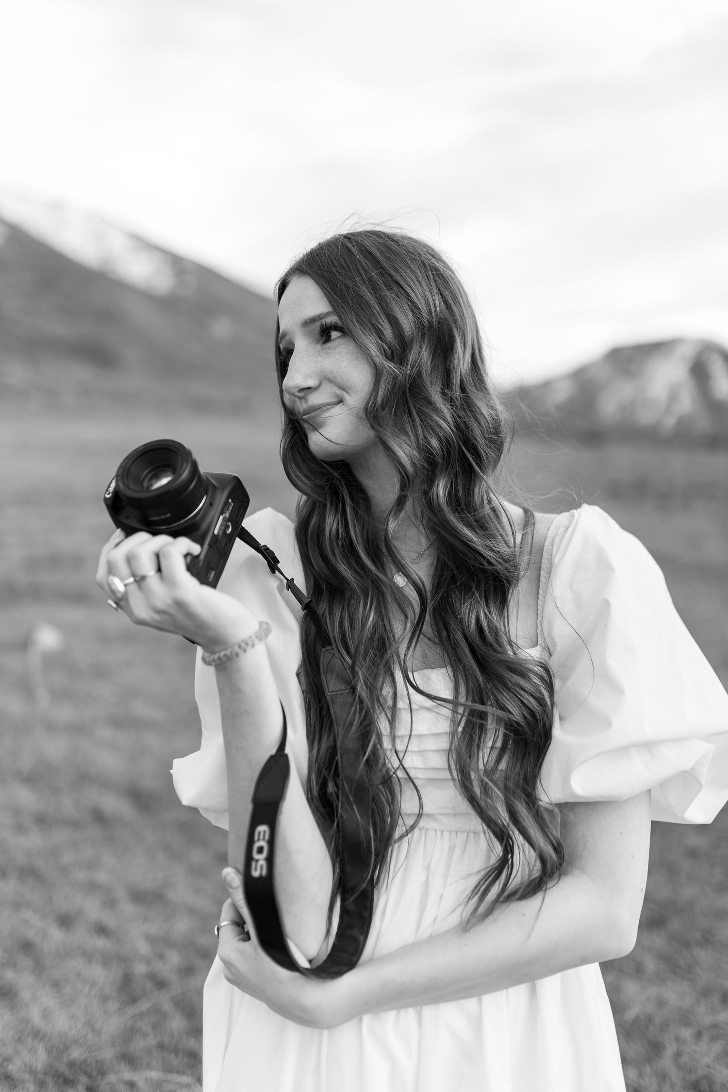 Person in white dress holding and playing with a black cat outdoors.