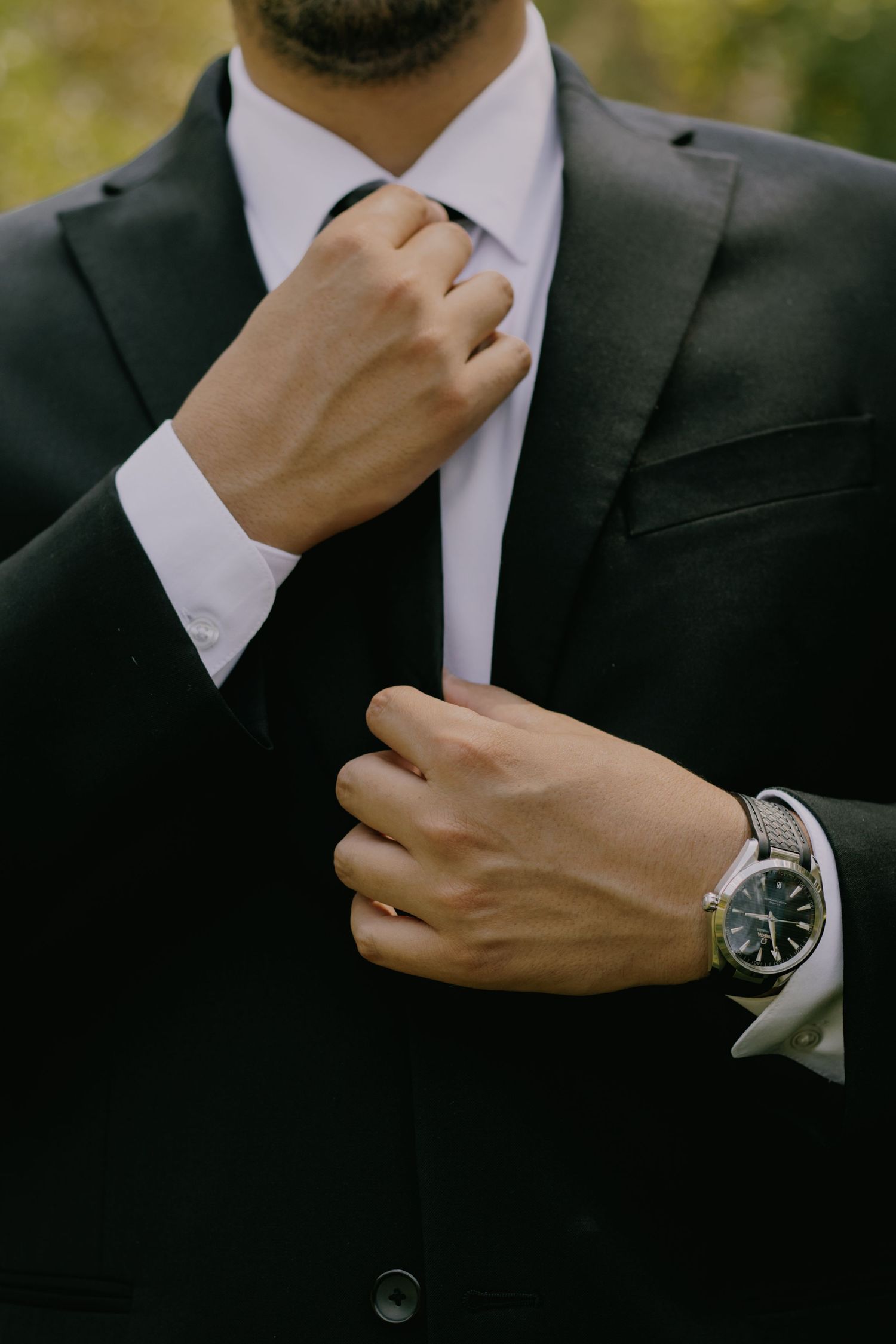 Close-up of hands adjusting a black suit tie with elegant wristwatch detail.