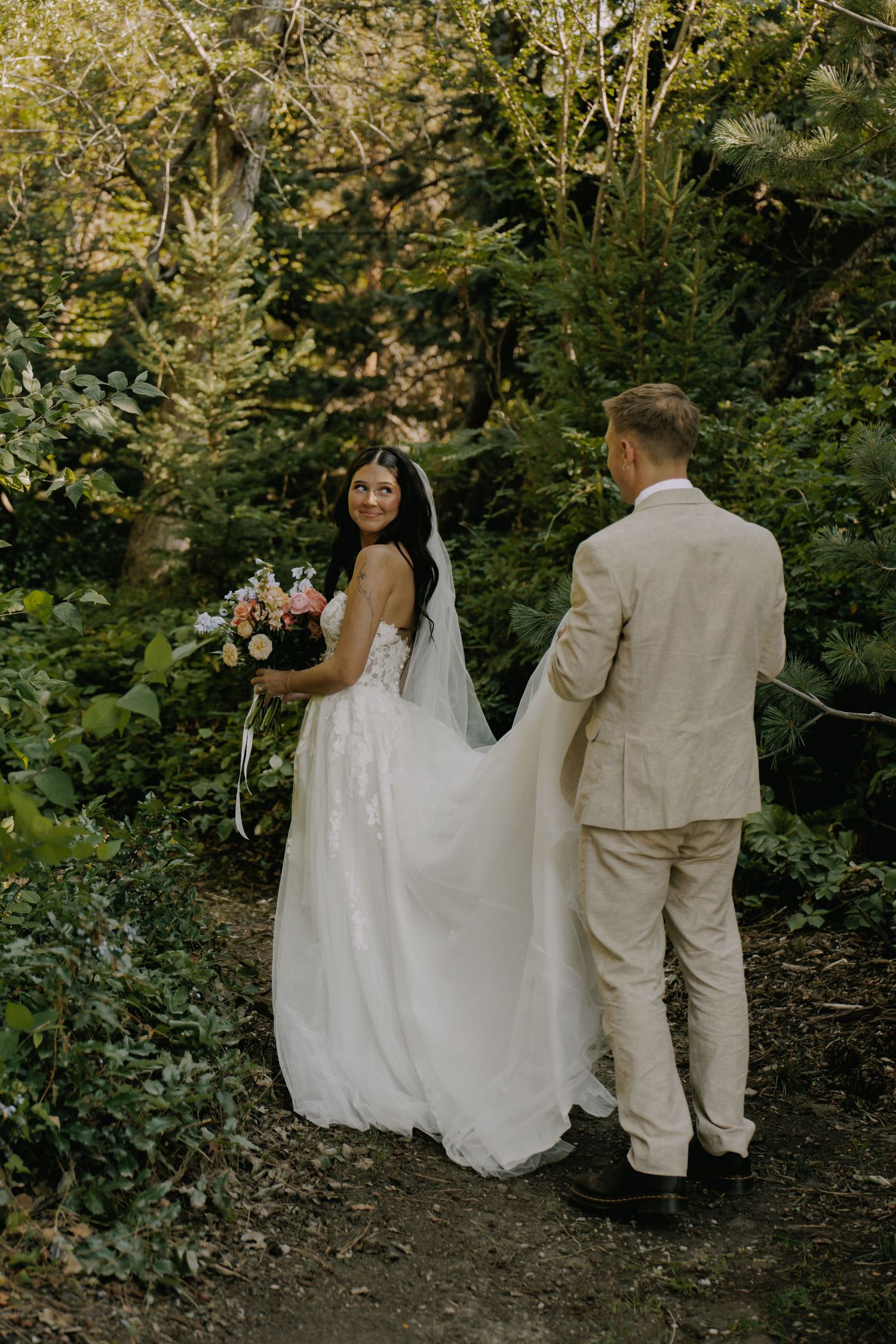 Wedding couple walking through a lush garden path in coordinated cream-colored attire.