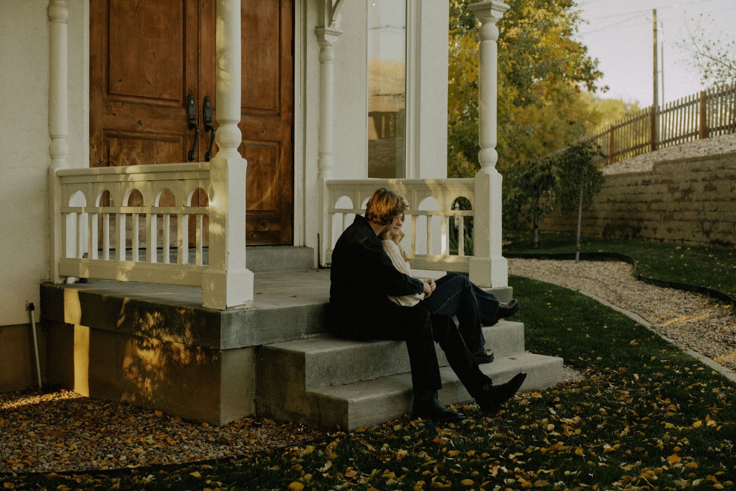 Autumn engagement session on a historic porch with fallen leaves.