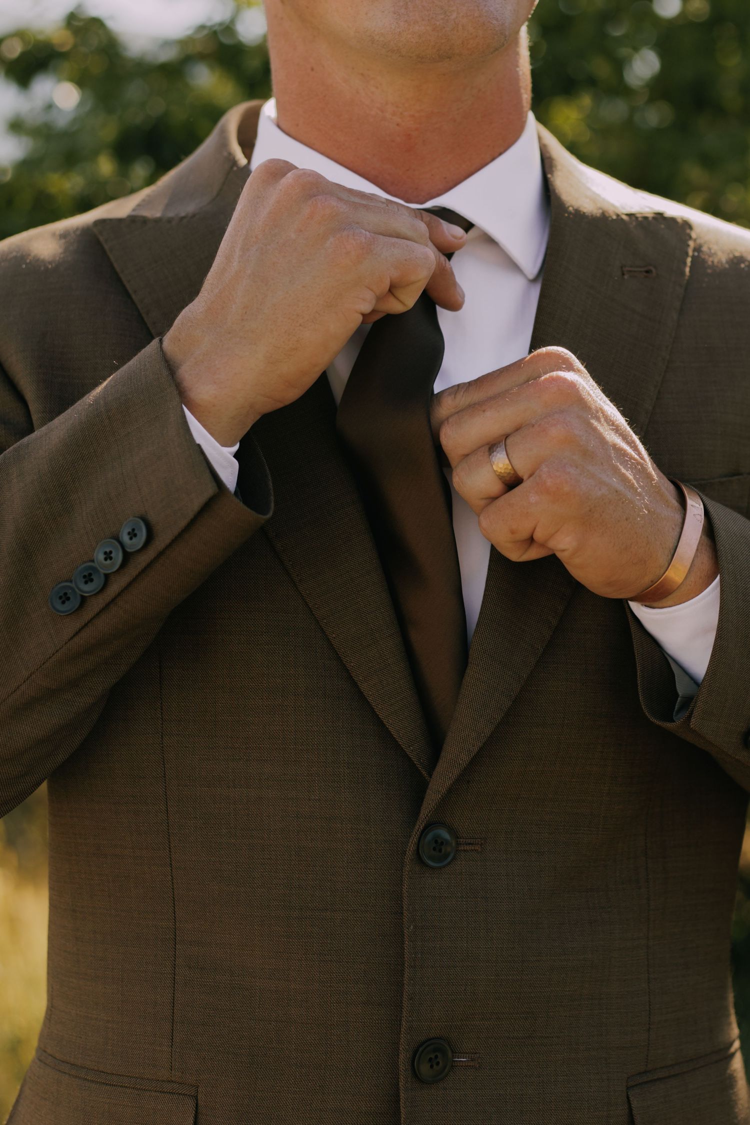 Close-up shots of groom adjusting brown suit and tie.