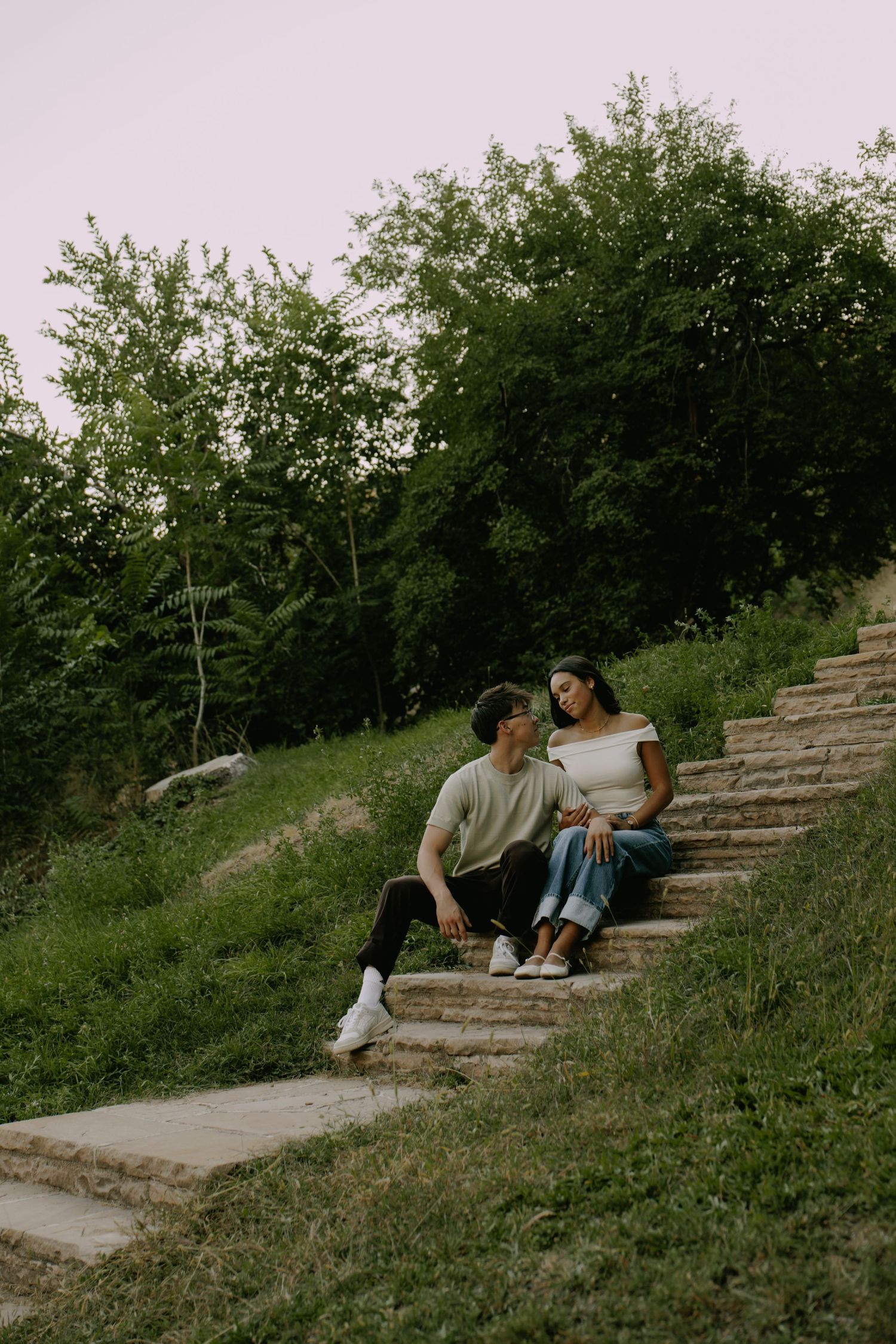 Couple sitting together on stone steps surrounded by lush greenery.