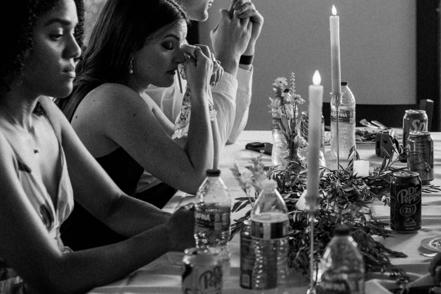 Black and white image of guests dining at an elegant table with candles and wine bottles.