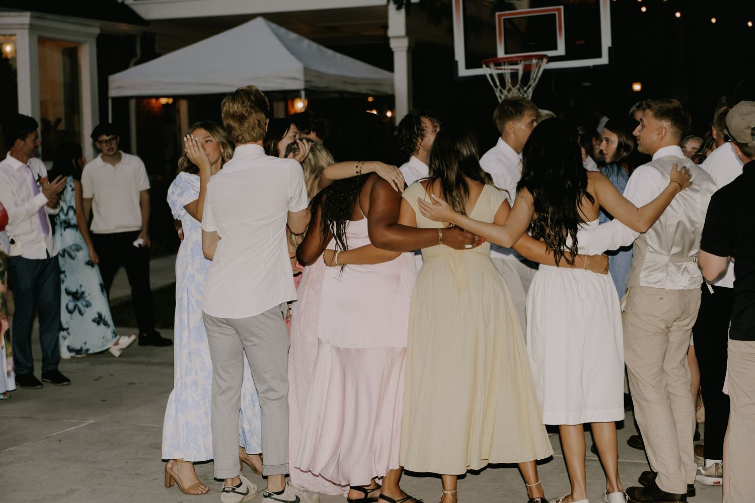 Outdoor wedding reception with basketball court and string lights visible in background.