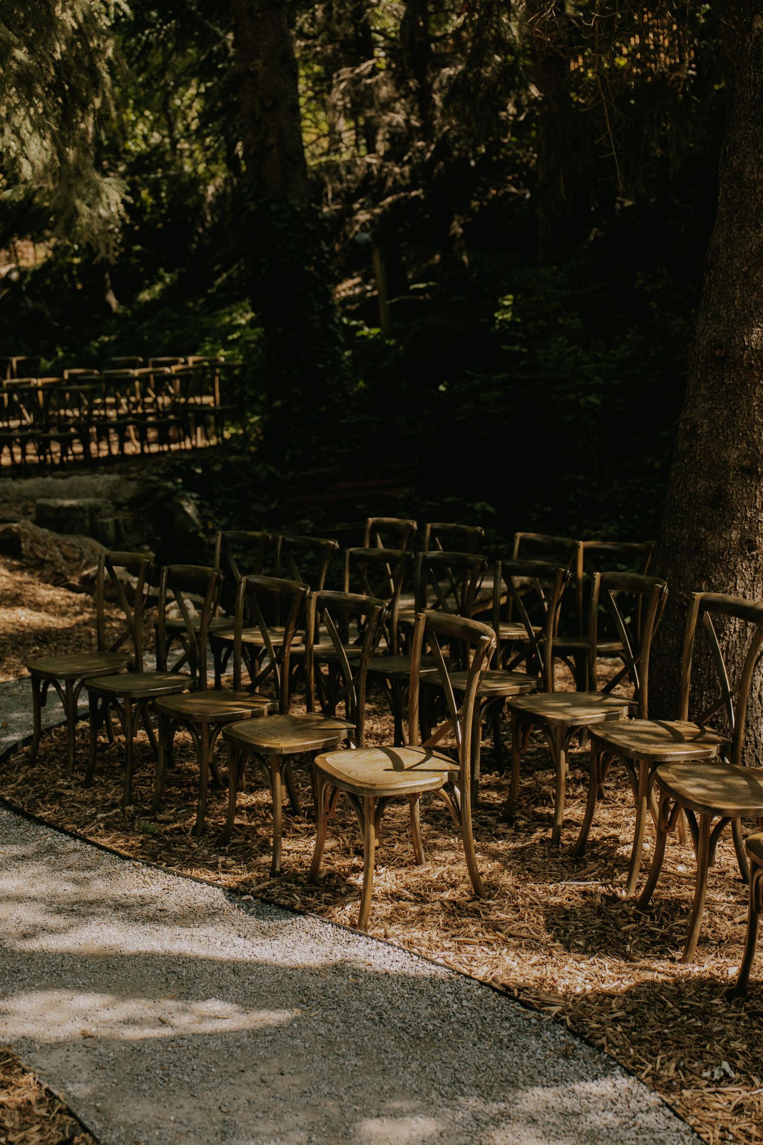Rows of wooden chairs arranged outdoors under trees for a wedding ceremony.