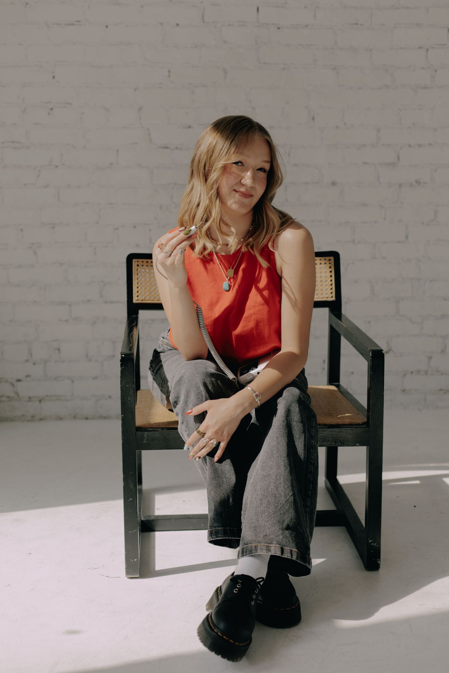 Casual portrait of someone seated in black frame chair wearing red top and jeans.