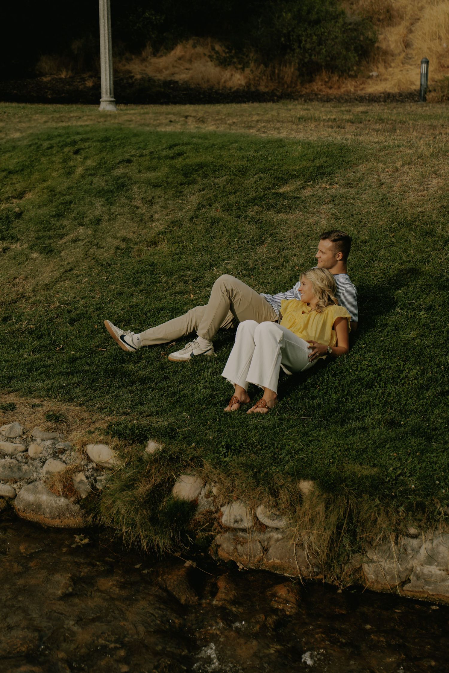A couple relaxes together on a grassy hillside during golden hour.