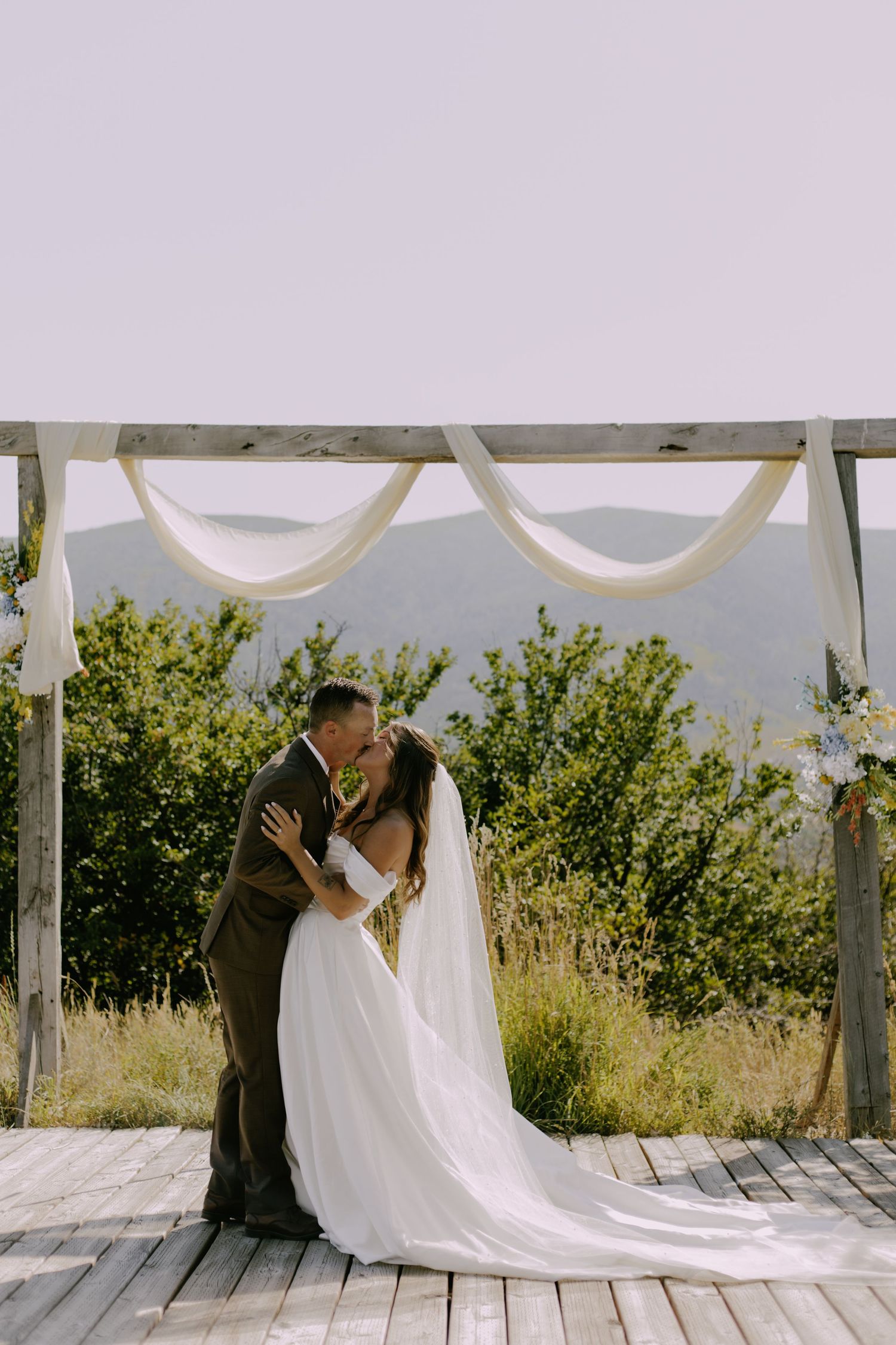 Wedding ceremony under a white draped pergola with mountain landscape backdrop.