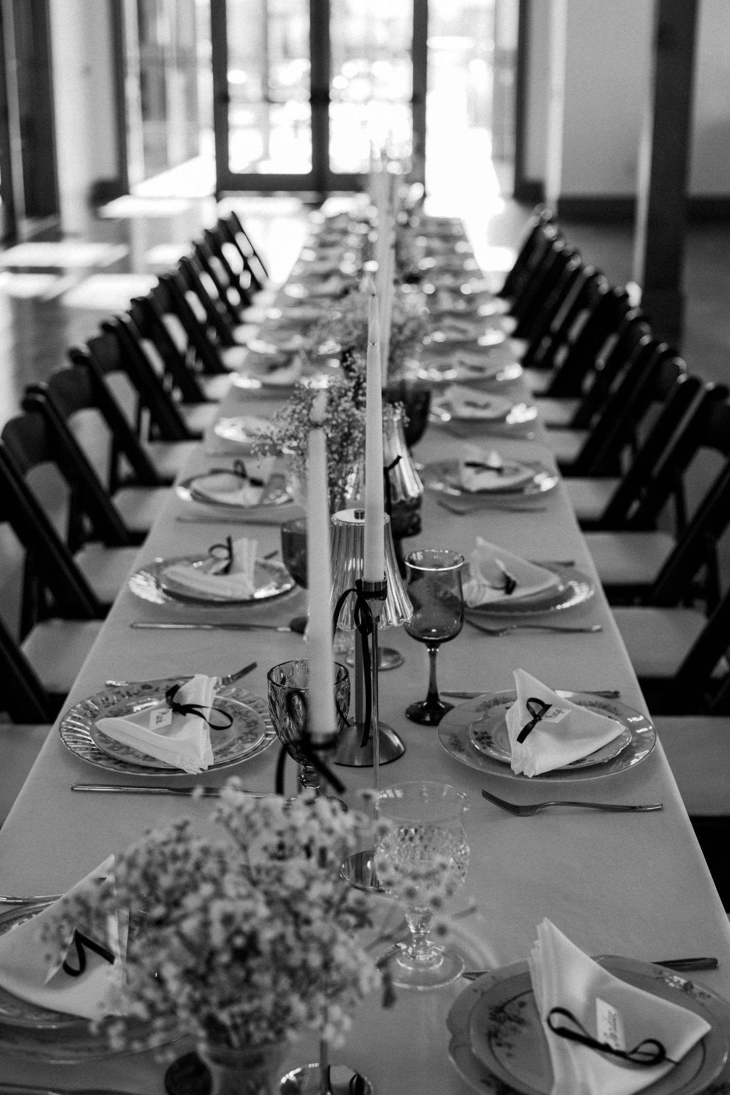 Black and white photo of a formal dining table setup with place settings and floral decorations.