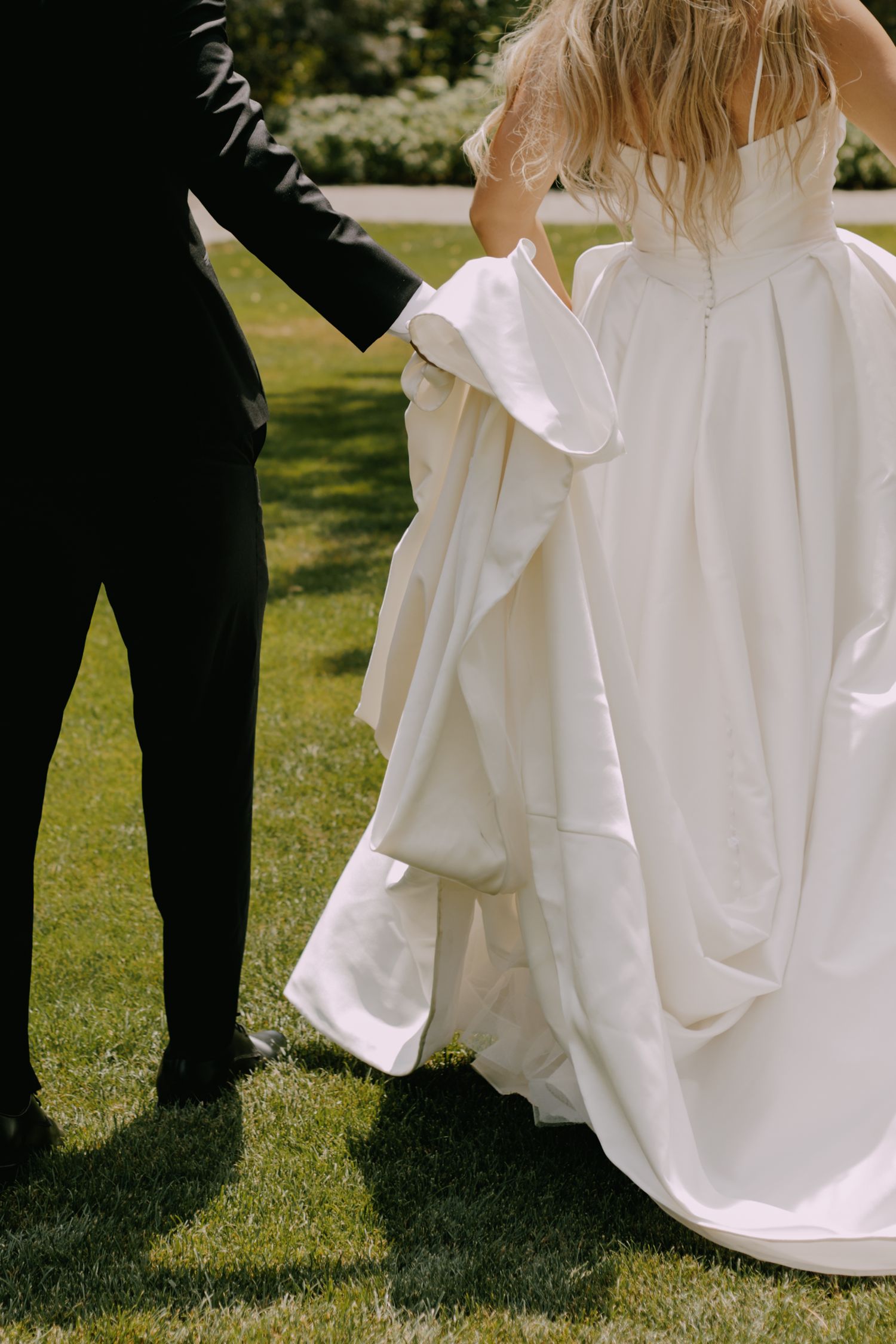 Detail shots of flowing white wedding dress against green grass.