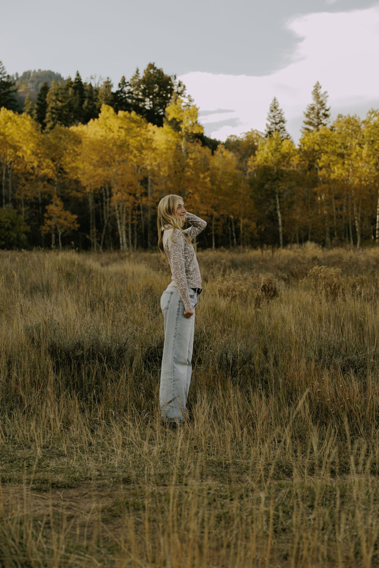 Person in light outfit poses in autumn field with golden aspen trees.