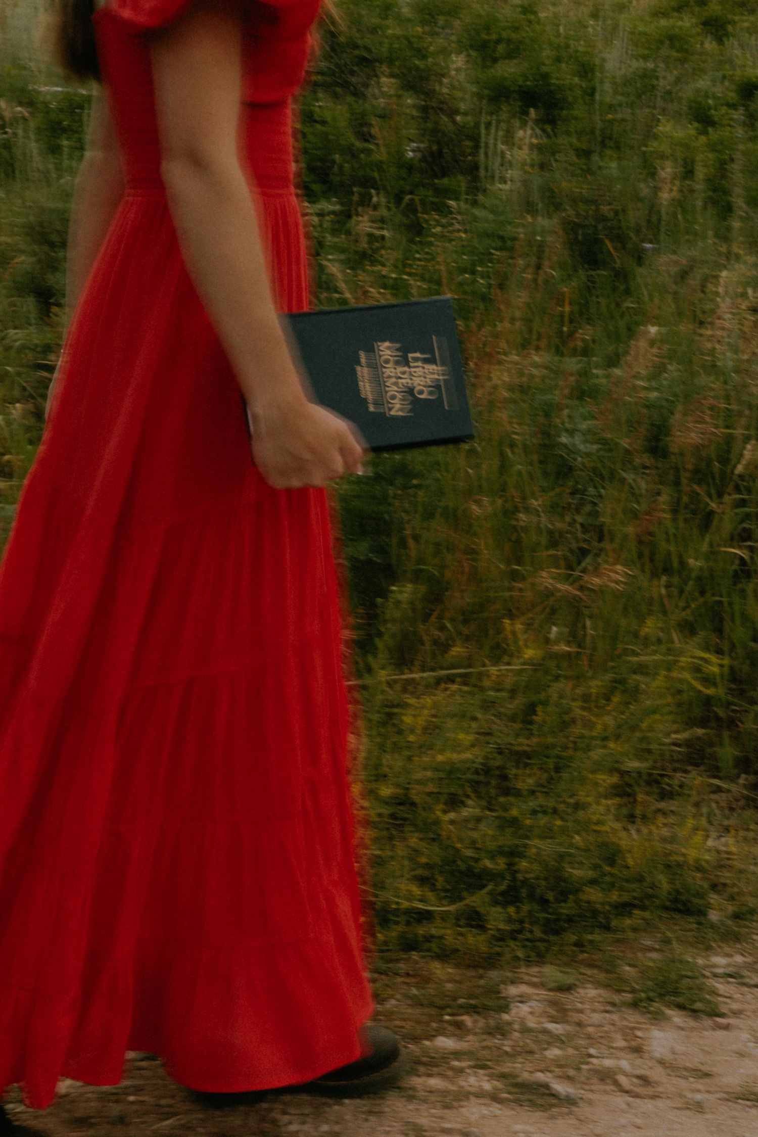 Someone wearing a vibrant red dress walks through tall grass in a natural setting.