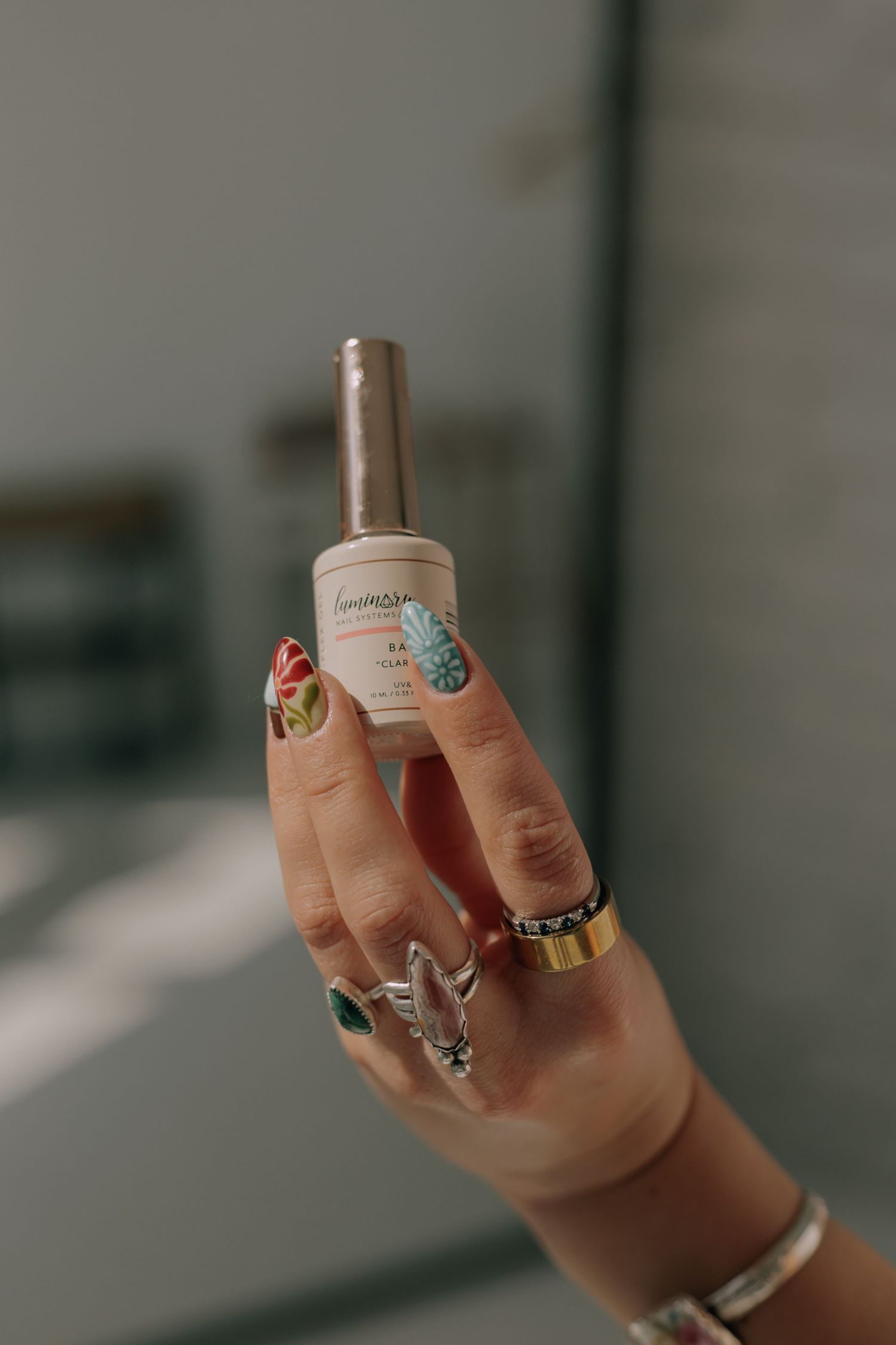 Close-up shot of hands wearing colorful rings and nail art against a blurred background.