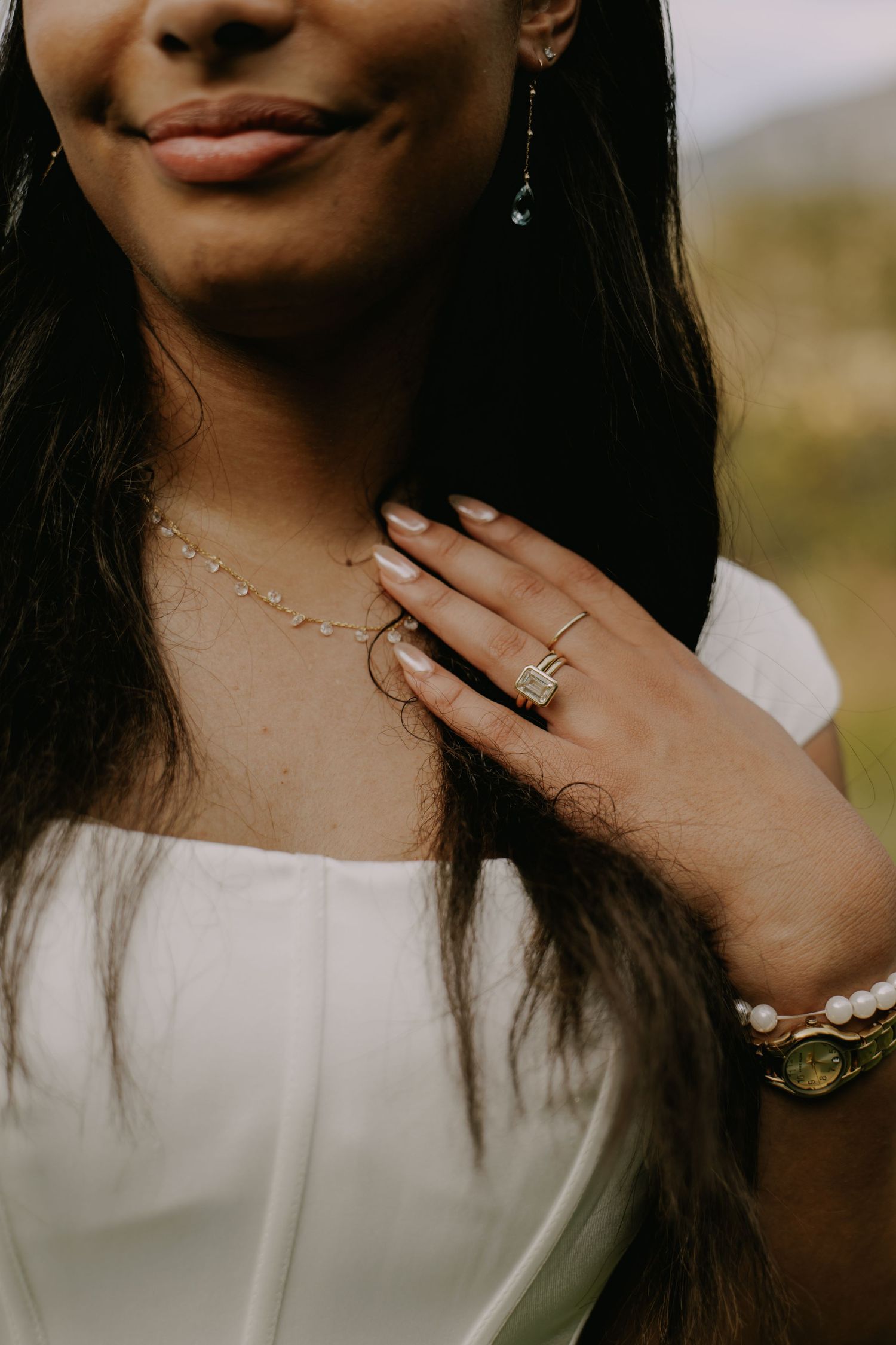 Close-up details of jewelry and hands against white fabric.