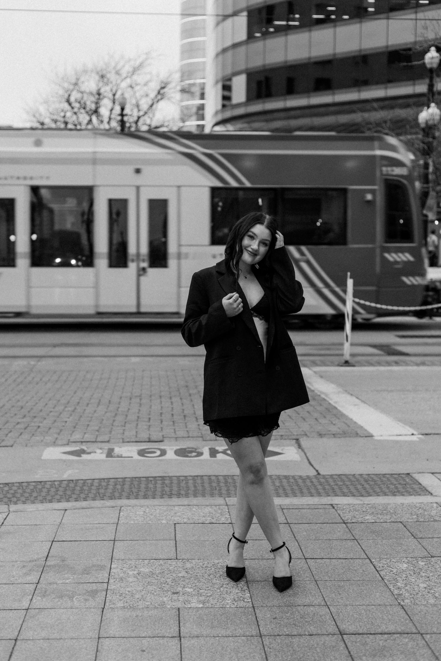 Black and white photo of person posing on urban sidewalk near modern building.