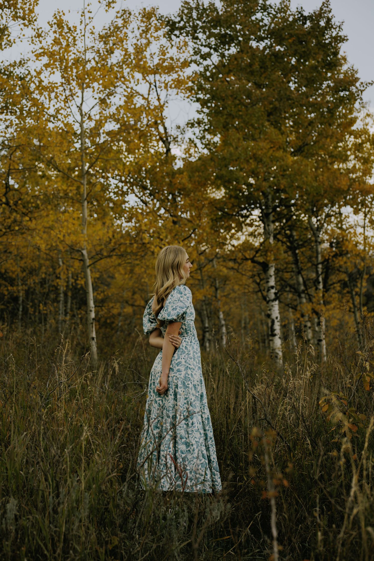 A blue floral dress flows gracefully against a backdrop of autumn trees and golden light.