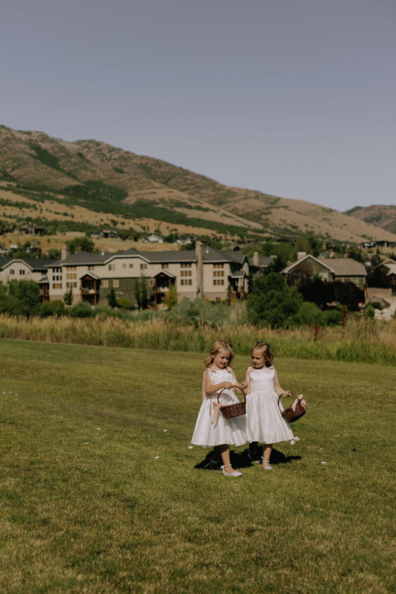 Wedding couple sitting in a grassy field with mountain landscape in the background.