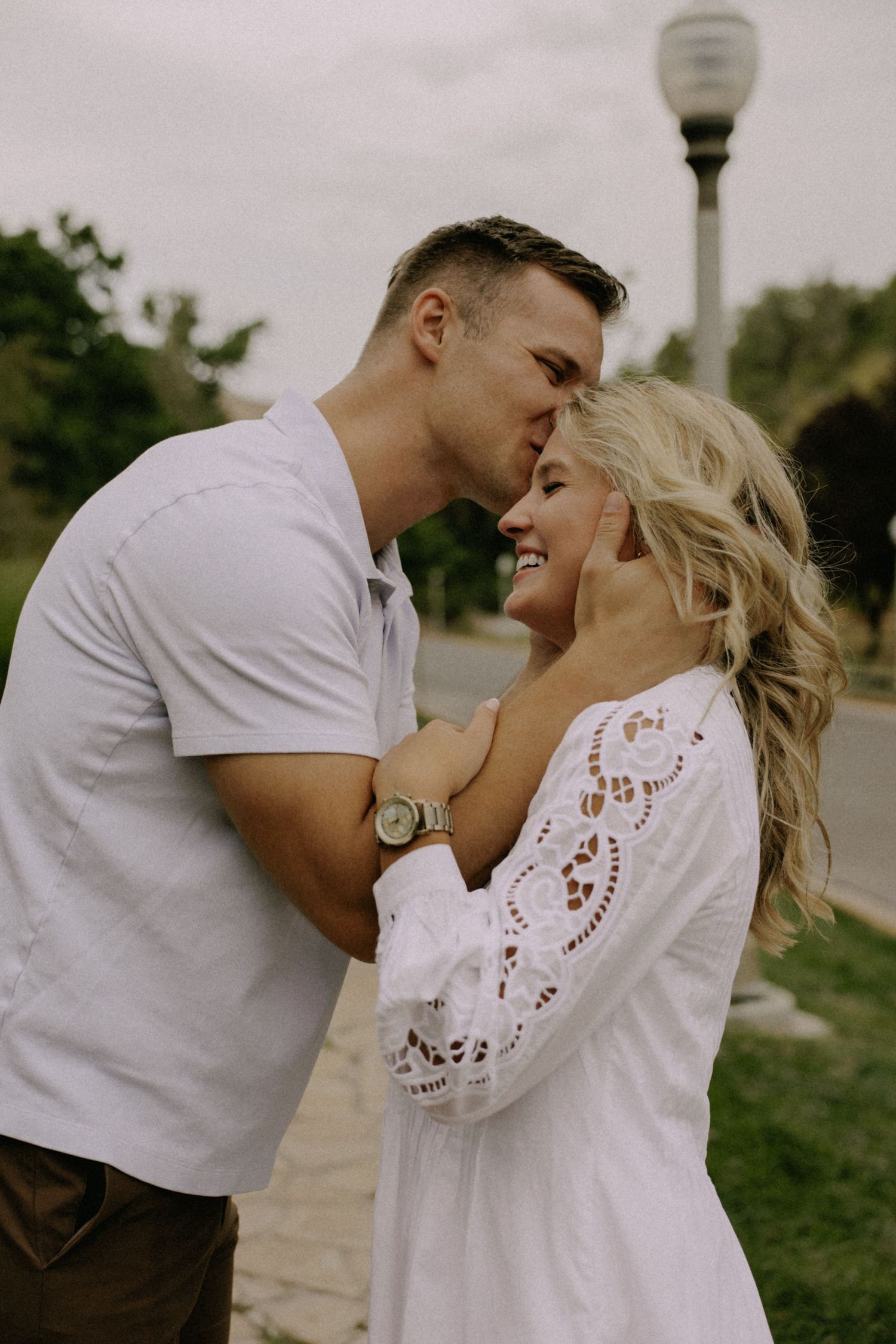 A couple shares an intimate moment near a lamppost in casual white clothing.