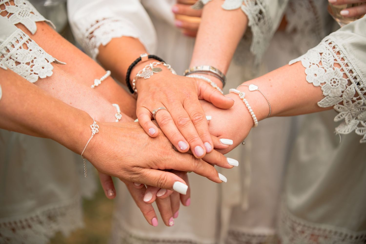 Bridesmaids and bride showing off white manicured nails and silver bracelets in matching robes.