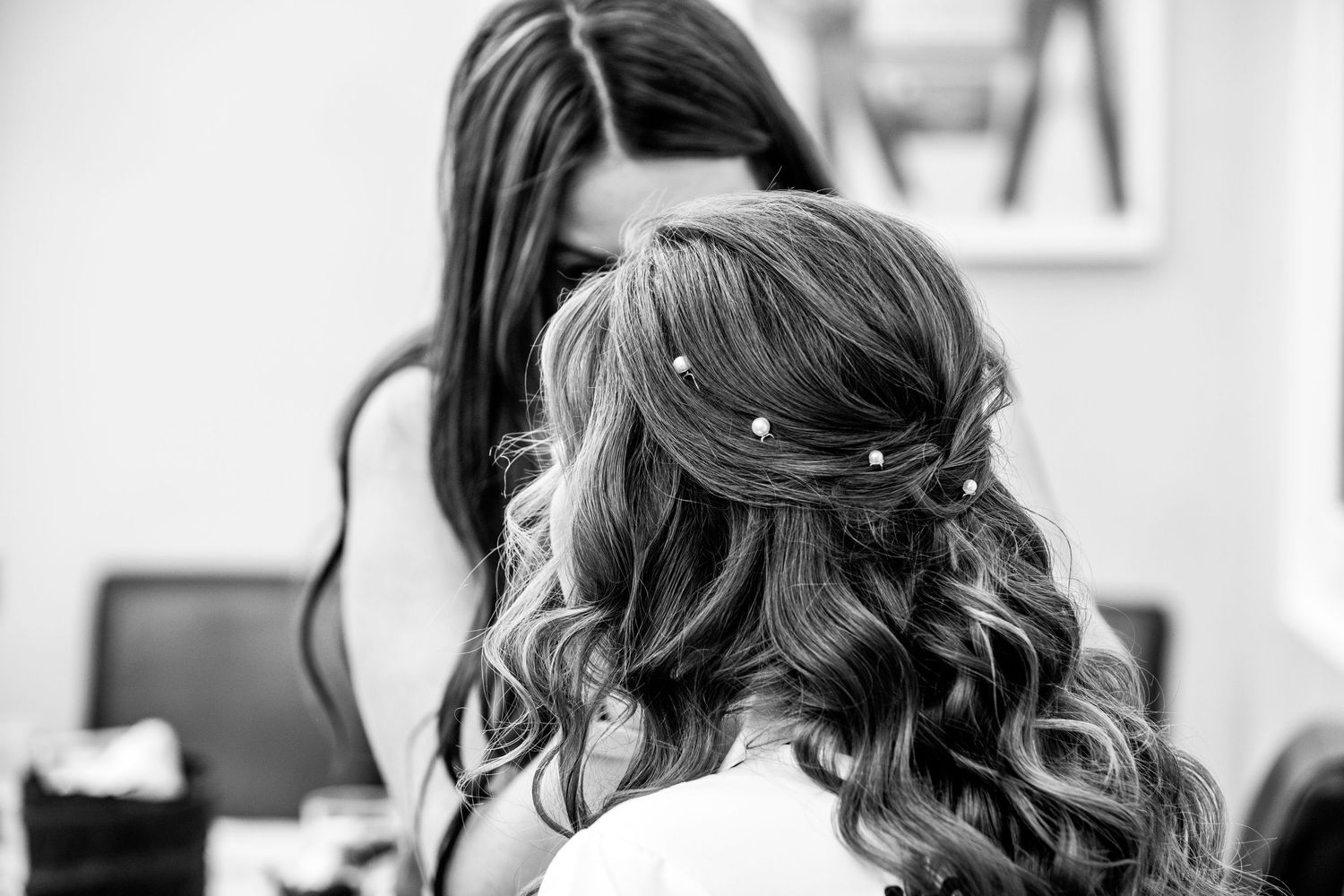 Black and white photo of bride having half-up hairstyle with pearl pins styled by hairdresser.