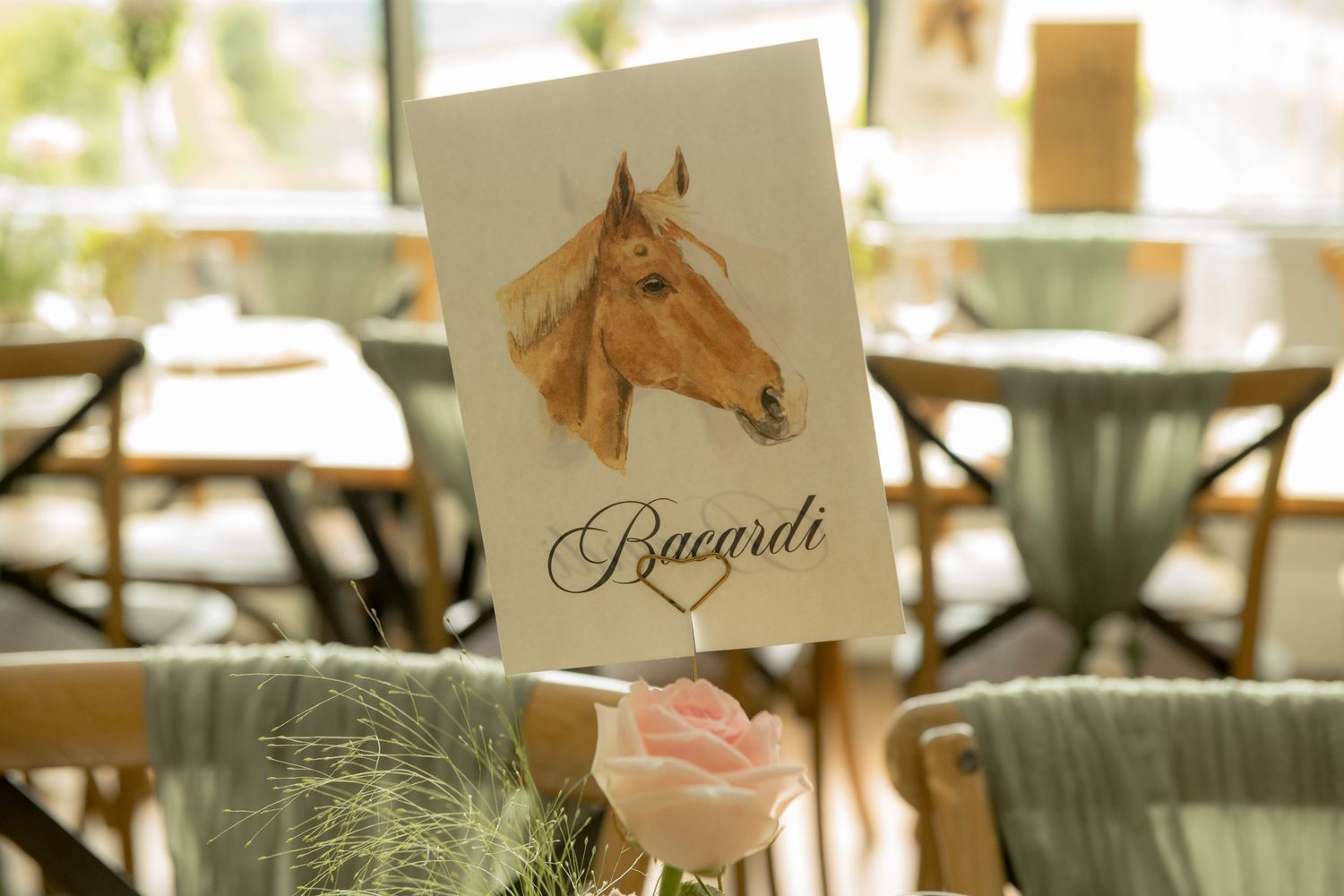 Wedding table name card featuring watercolor horse portrait labeled Bacardi with pink rose decor.