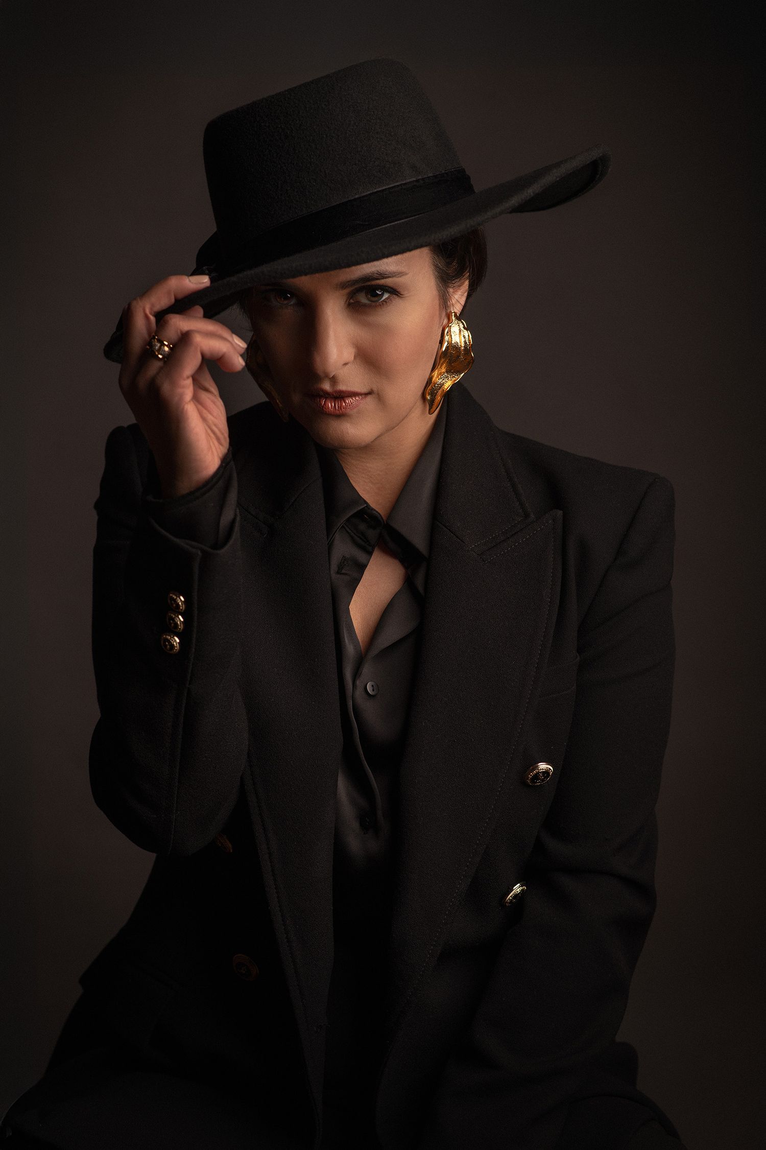 Stylish black and white portraits of persian pop singer Rana Mansour wearing black suit jacket and fedora hat in dark studio setting.