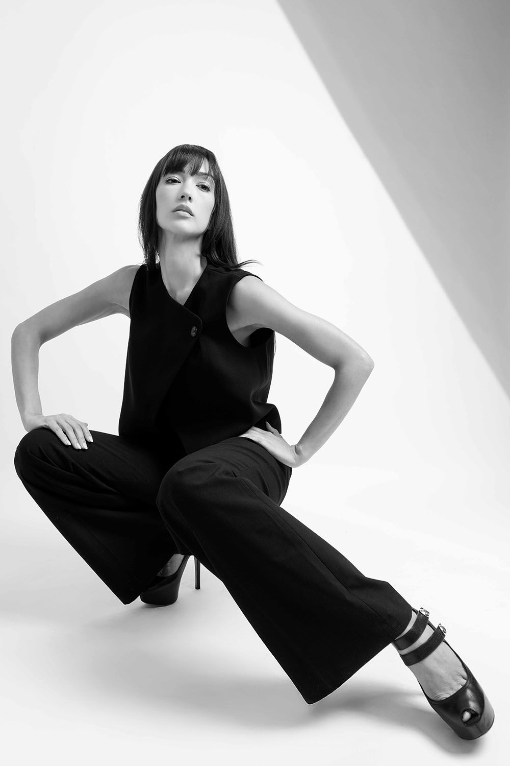 Black and white fashion photo of a woman in wide-leg pants and heels posing confidently in a studio.