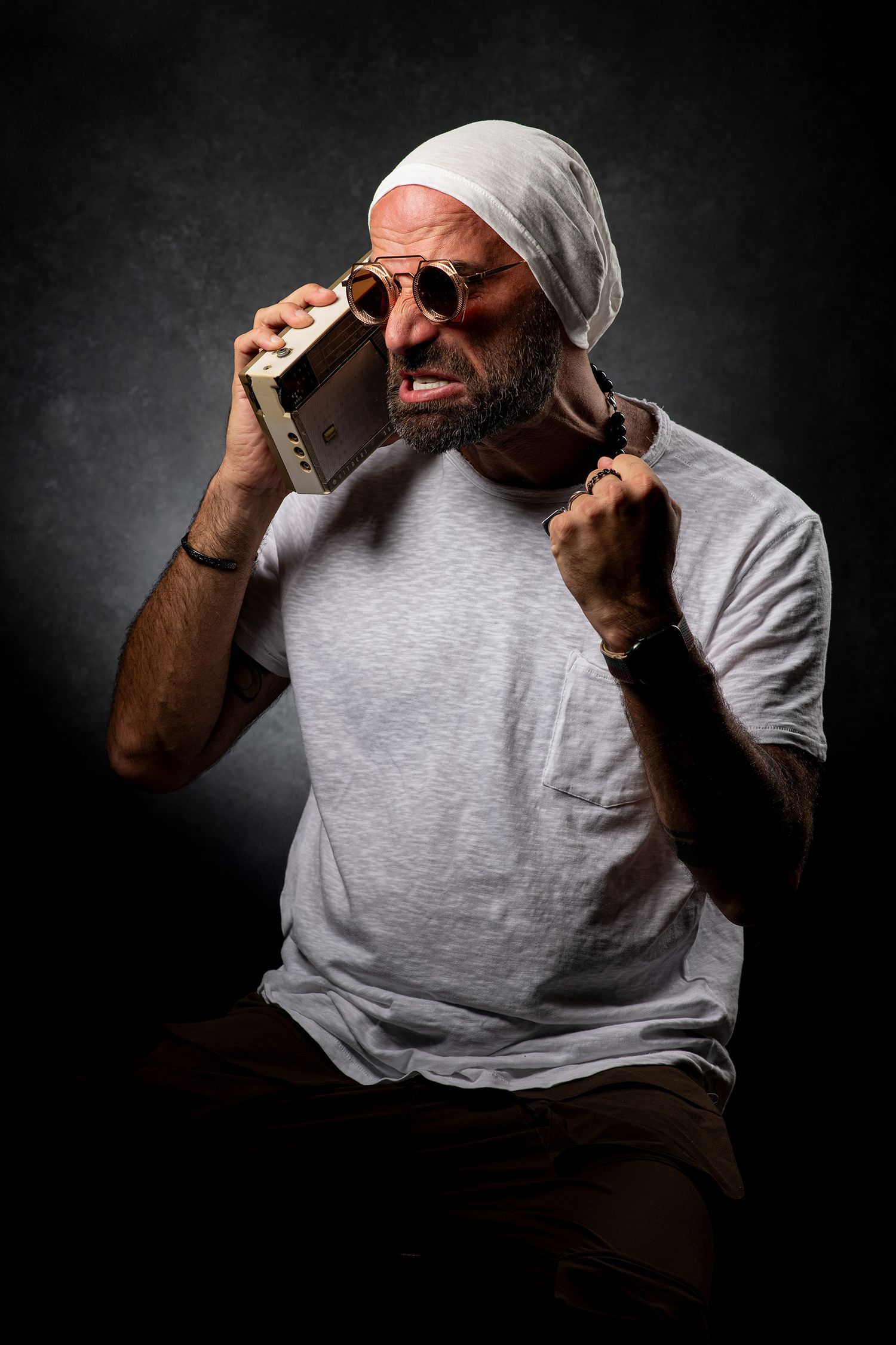 persian podcaster and comedian Farshid Manafi in gray shirt making dynamic gestures against dramatic black background.