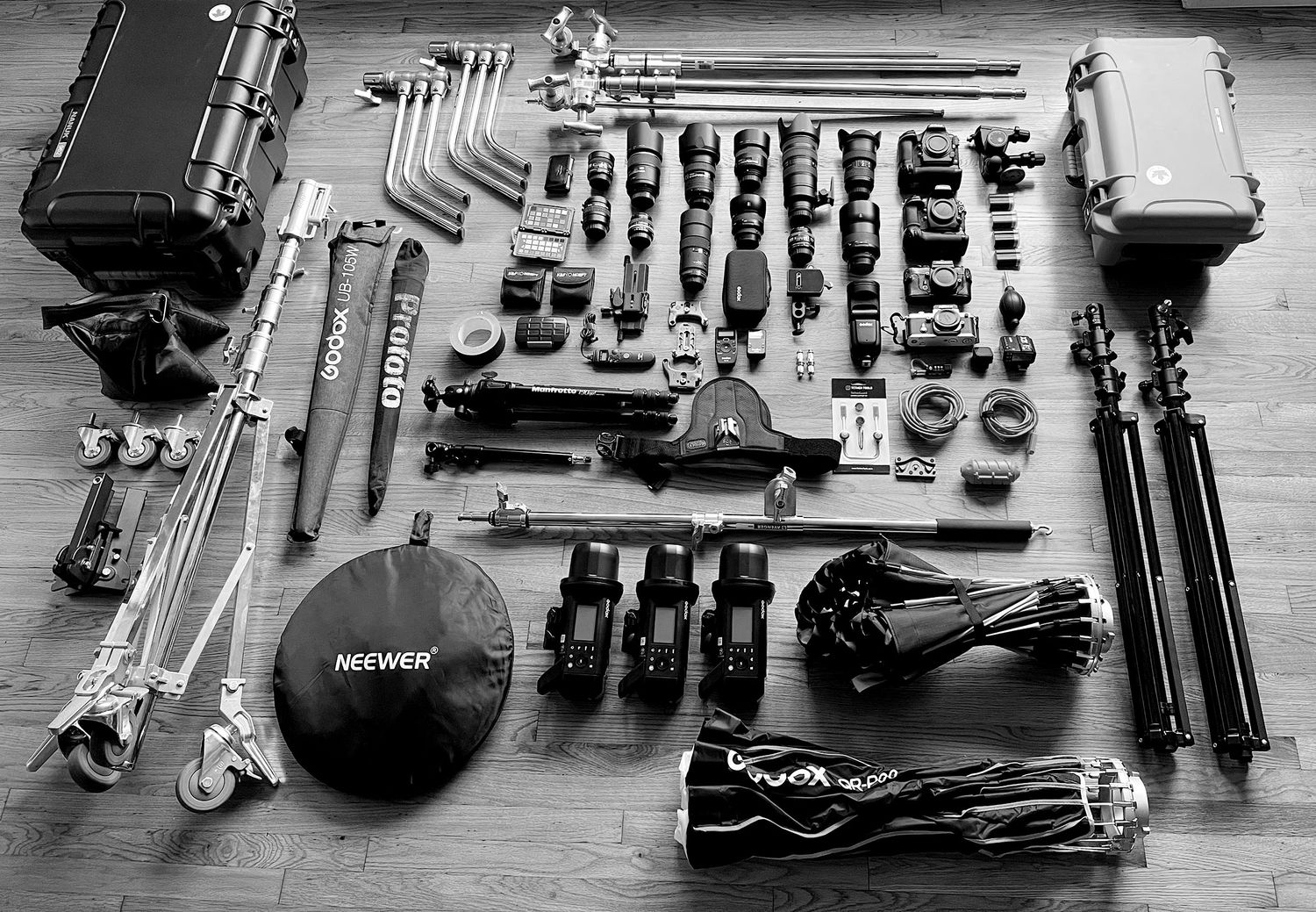 A black and white photo series showing organized collections of camera equipment laid out neatly on wooden surfaces.