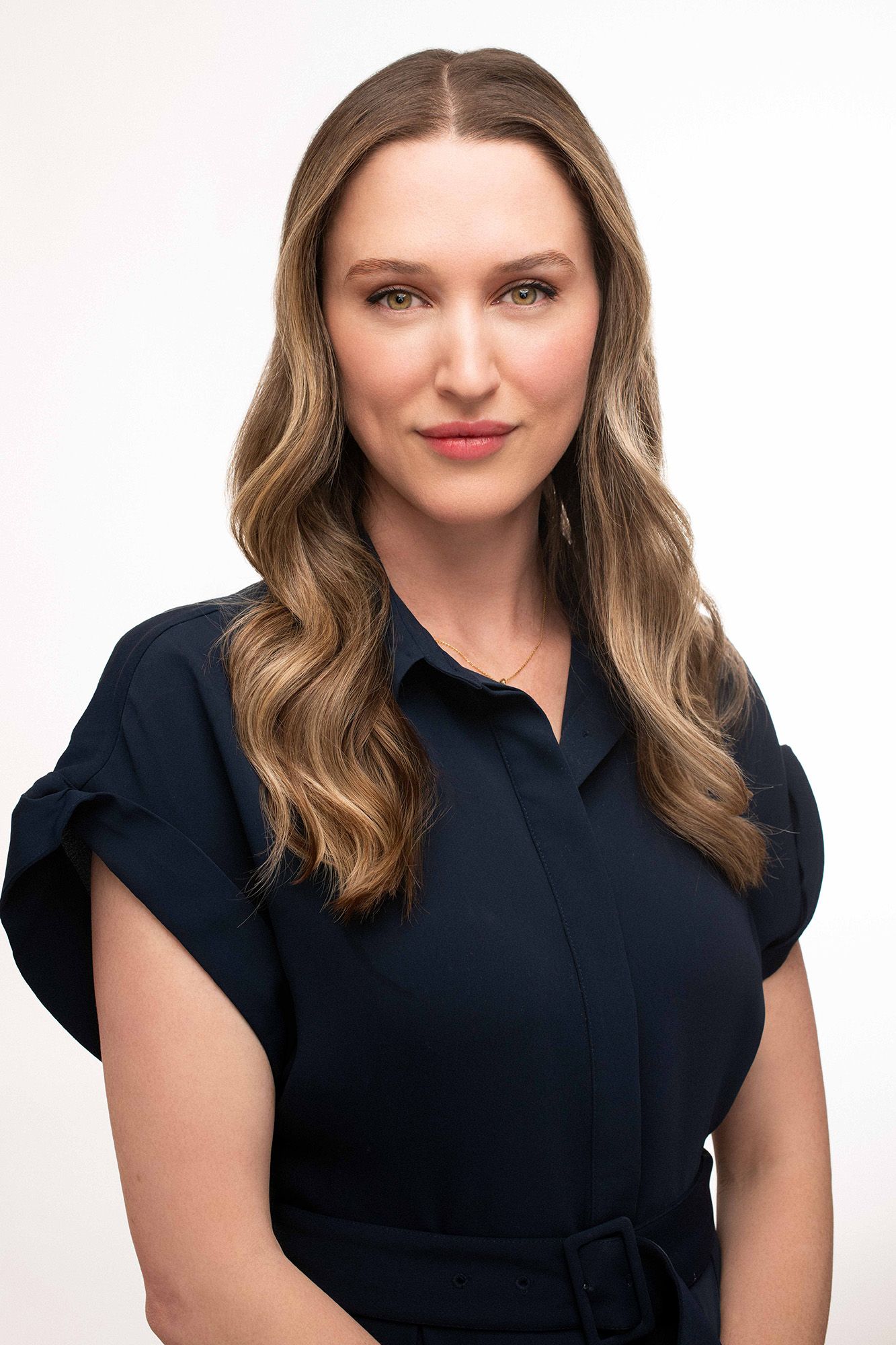 Professional headshot of a woman with wavy blonde hair wearing a navy blue dress, posing against a white background.