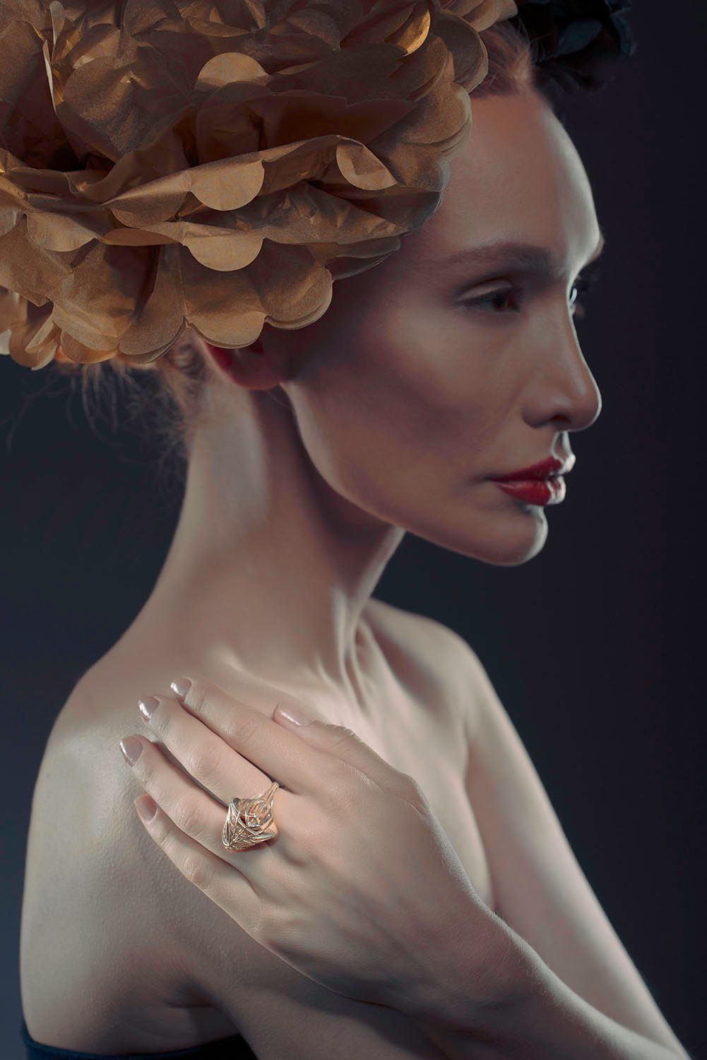 Woman in profile wearing an ornate floral headpiece and decorative gold ring on her shoulder.