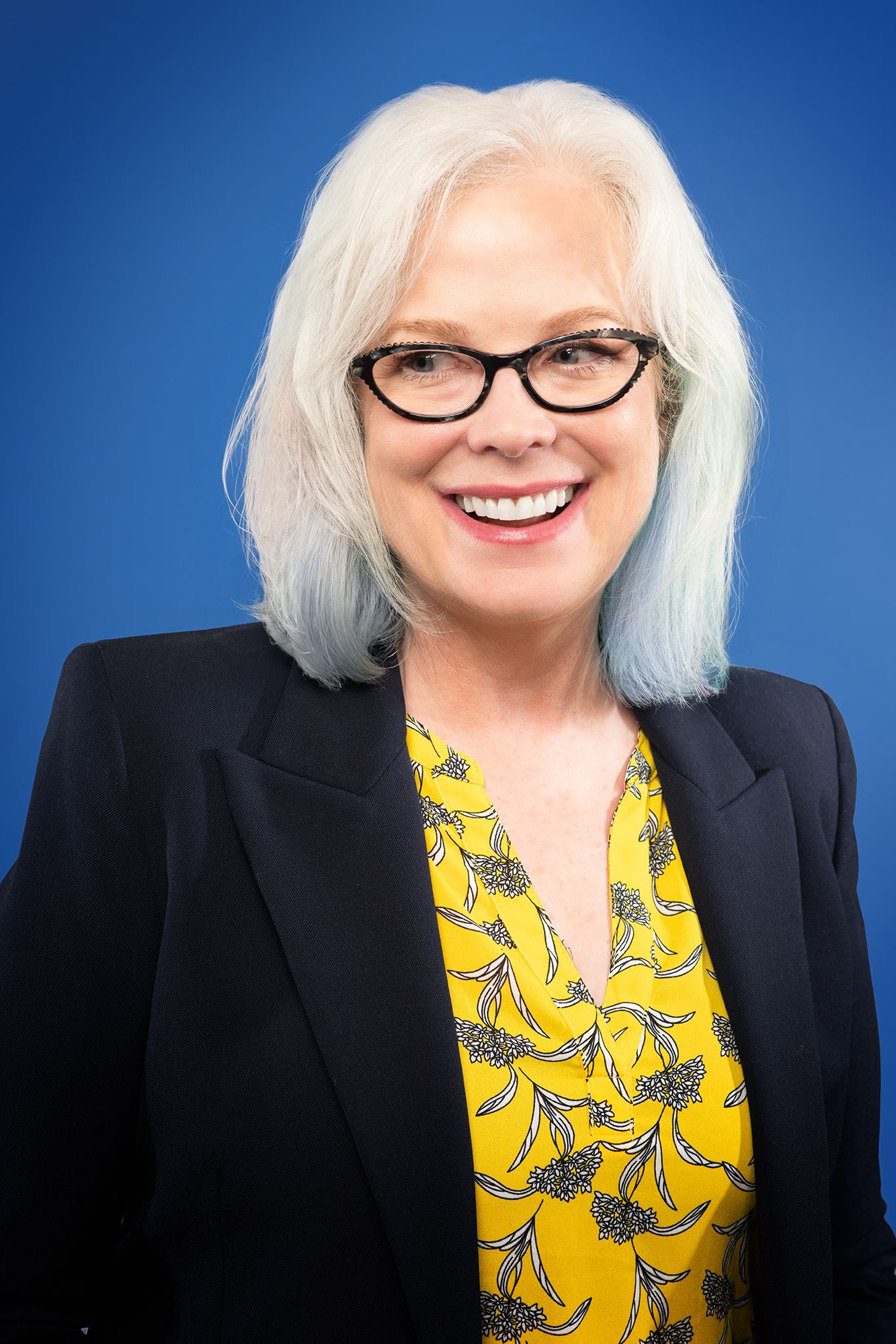 casting headshot Portrait sequence featuring a woman in glasses and black jacket with bright yellow floral blouse against blue background.