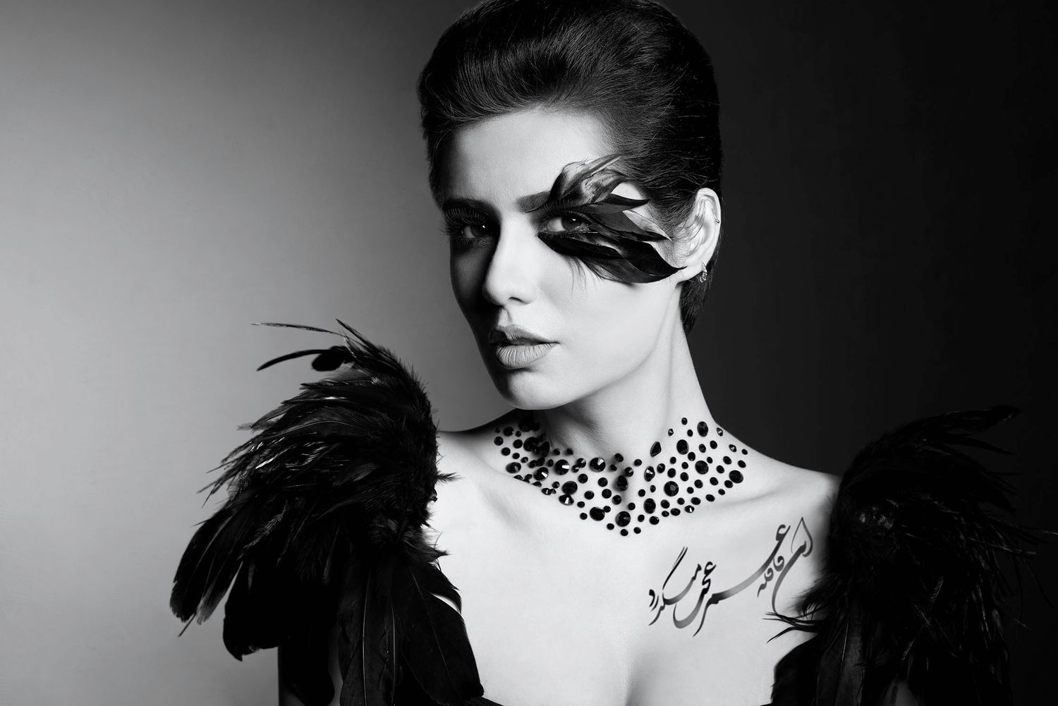 Black and white fashion portrait of a woman with dramatic feather accessories and jeweled necklace.