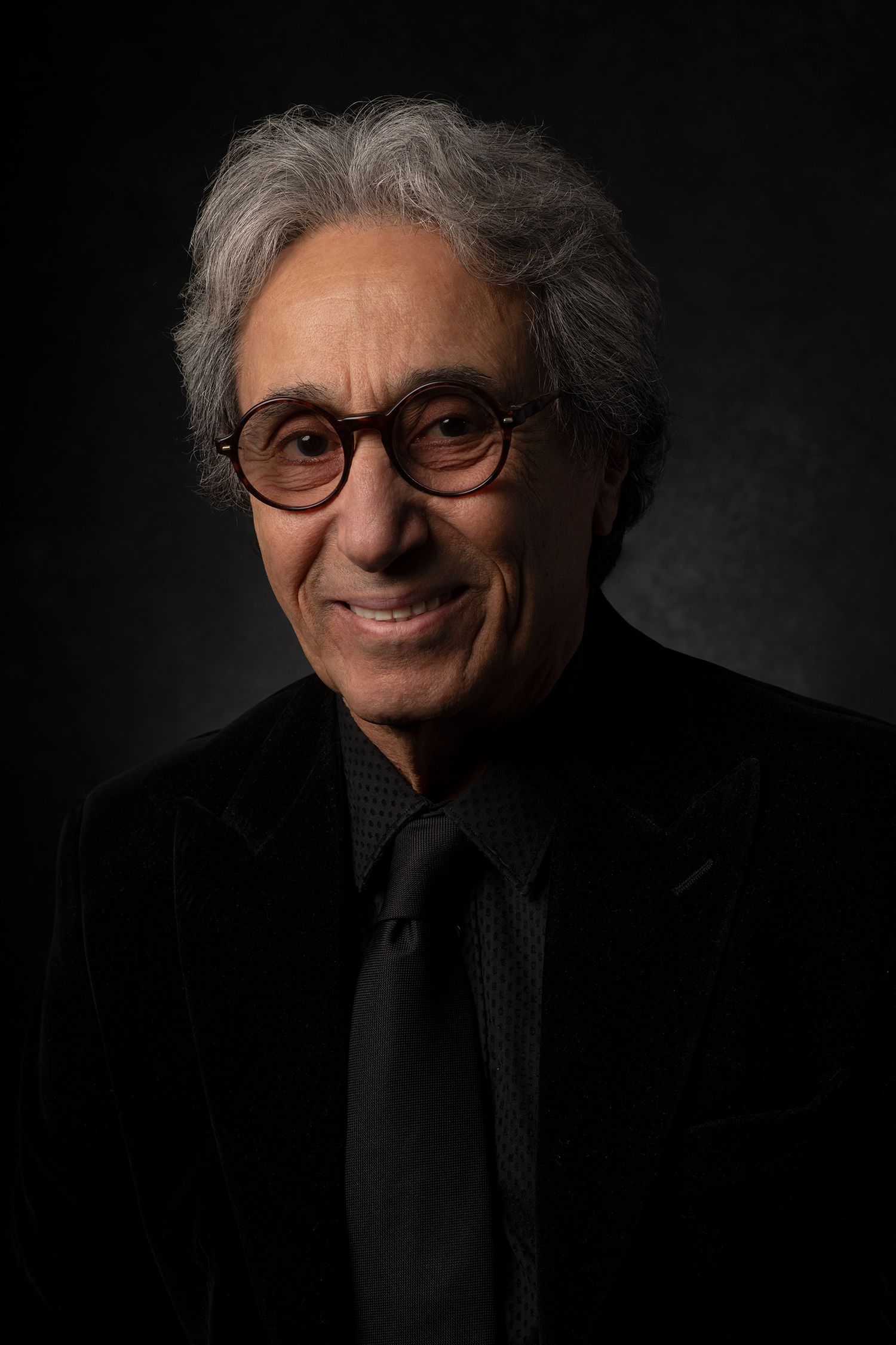 Candid studio portraits of smiling persian pop singer Shahbal Shabpareh with silver hair and glasses in black attire Westwood Los Angeles.