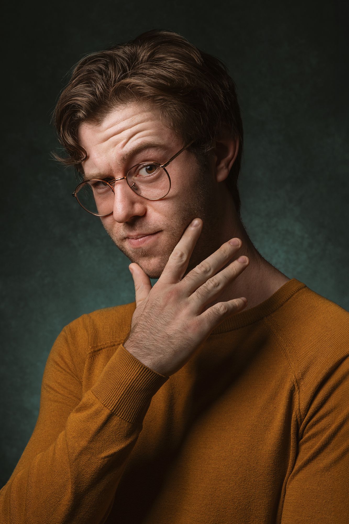 Casting headshot and portrait of person in mustard sweater with glasses striking thoughtful pose against dark backdrop taken in west LA.